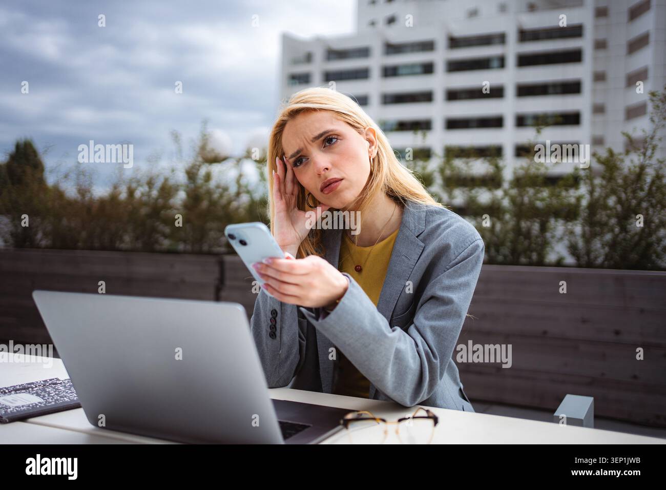 Stressed young woman working remotely outdoors using smartphone Stock Photo