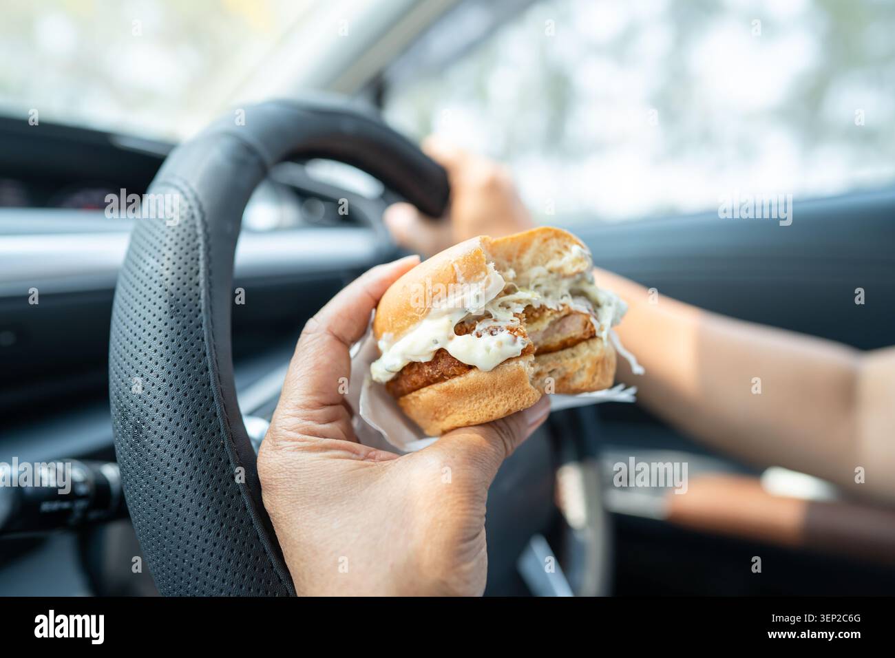 Asian lady holding hamburger to eat in car, dangerous and risk an accident. Stock Photo