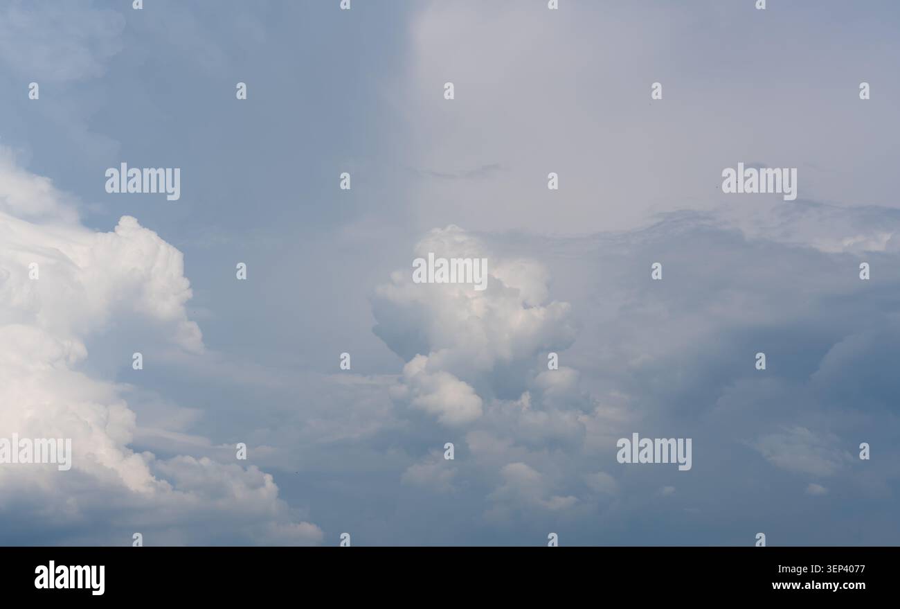Soft clouds drift above a calm, pale blue sky Stock Photo