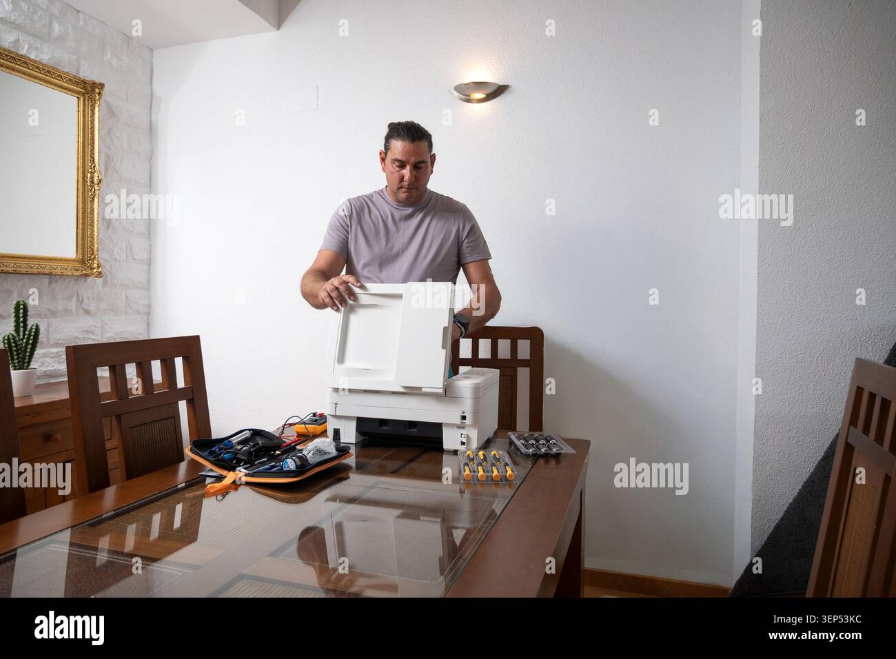Man opening a printer for maintenance on a dining table with various tools Stock Photo