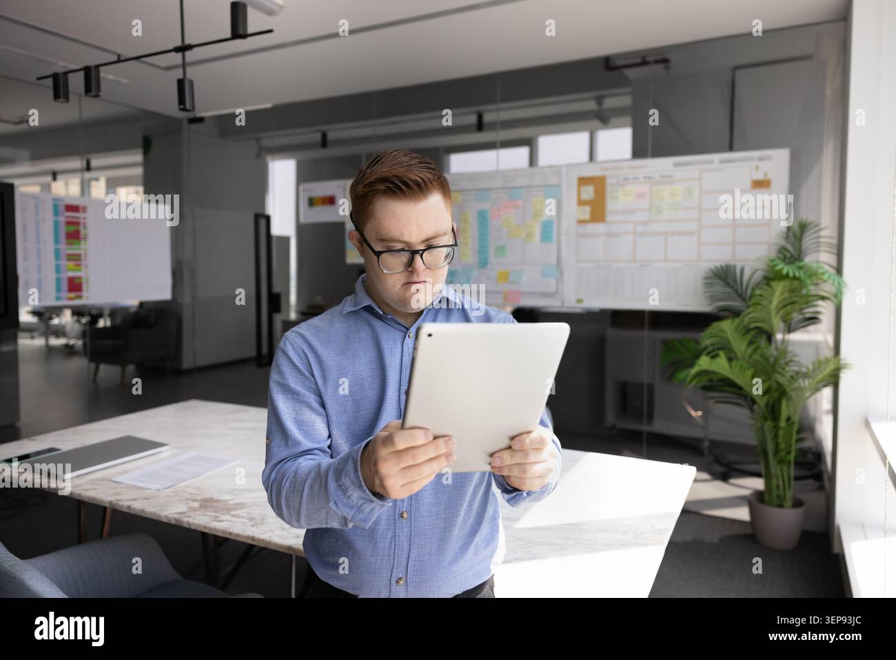 Young man with Down syndrome using tablet in office Stock Photo