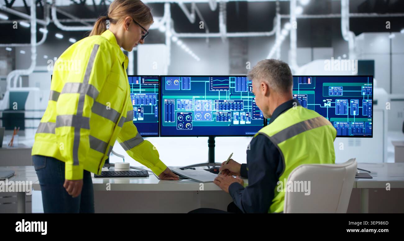 Two Factory Workers Discuss Production Changes During Busy Shift Handover. Stock Photo