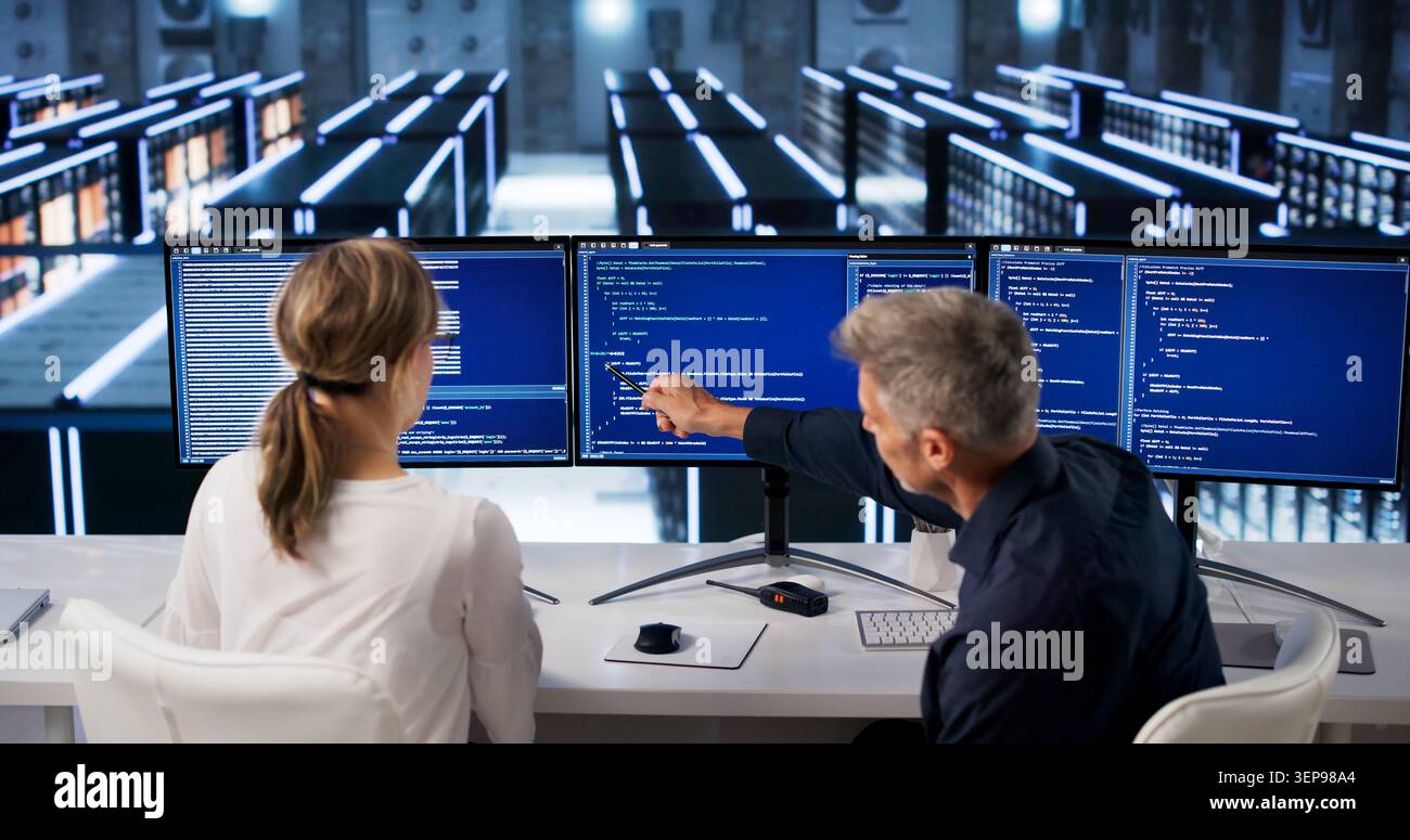 Two Programmers Typing On Computers In Big Data Center Room Managing Servers. Stock Photo