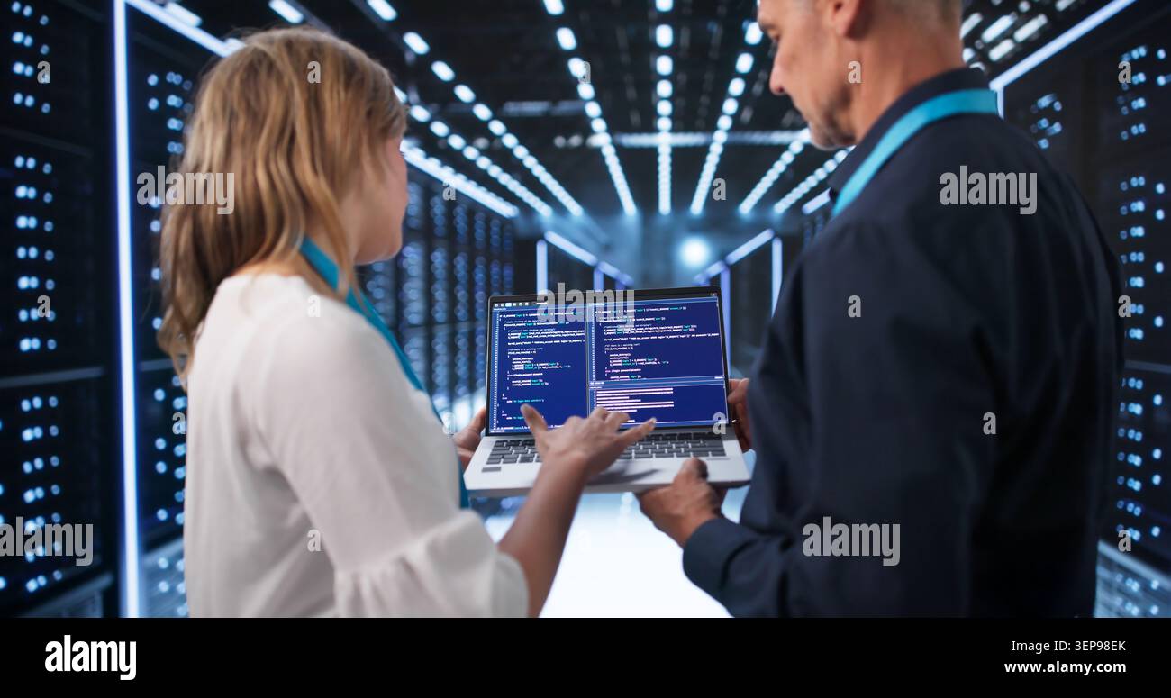 Two Engineers Analyzing Cloud Servers On Laptops In Modern Data Center. Stock Photo