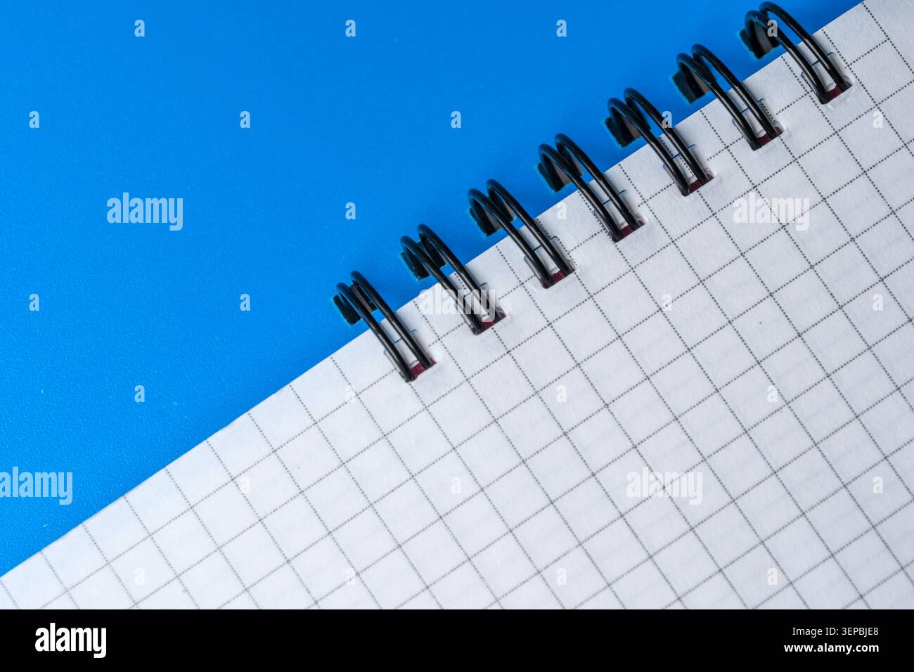 A blank grid notebook lies open, inviting ideas on a vibrant blue surface. Stock Photo