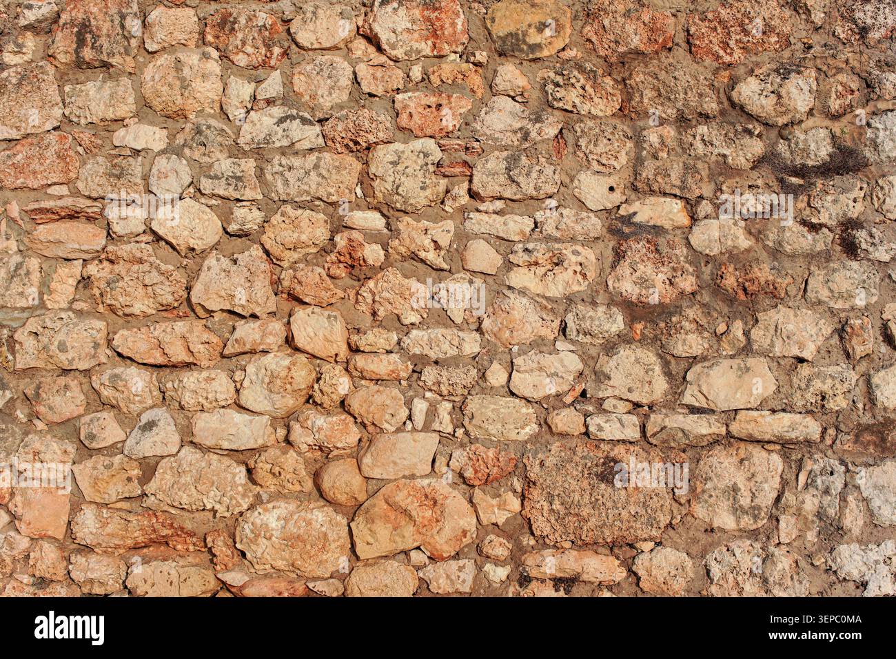 Rough reddish color stone bricks wall, sun shines on Stock Photo
