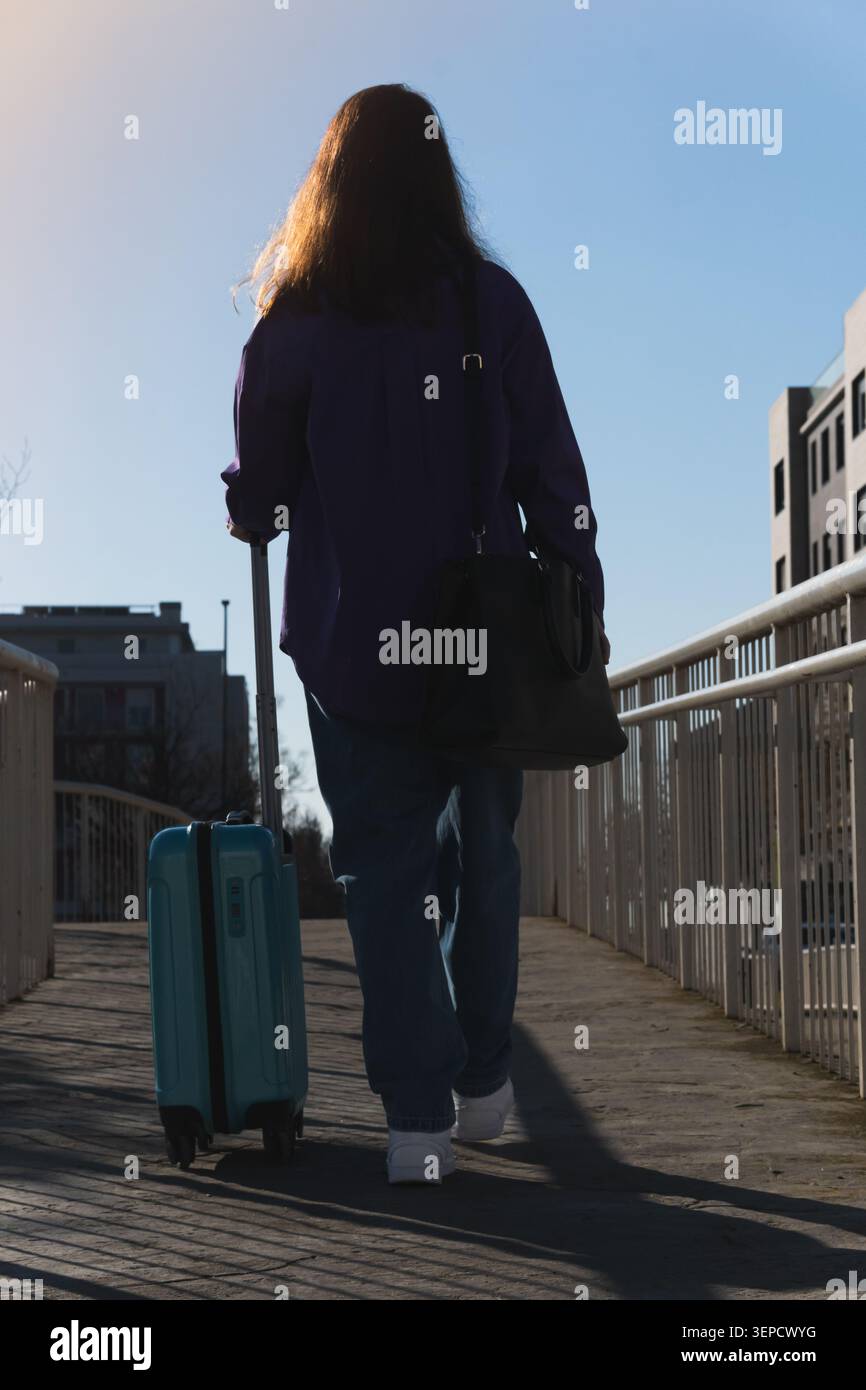 Woman pulling a light blue suitcase moving forward on a sunny day Stock Photo
