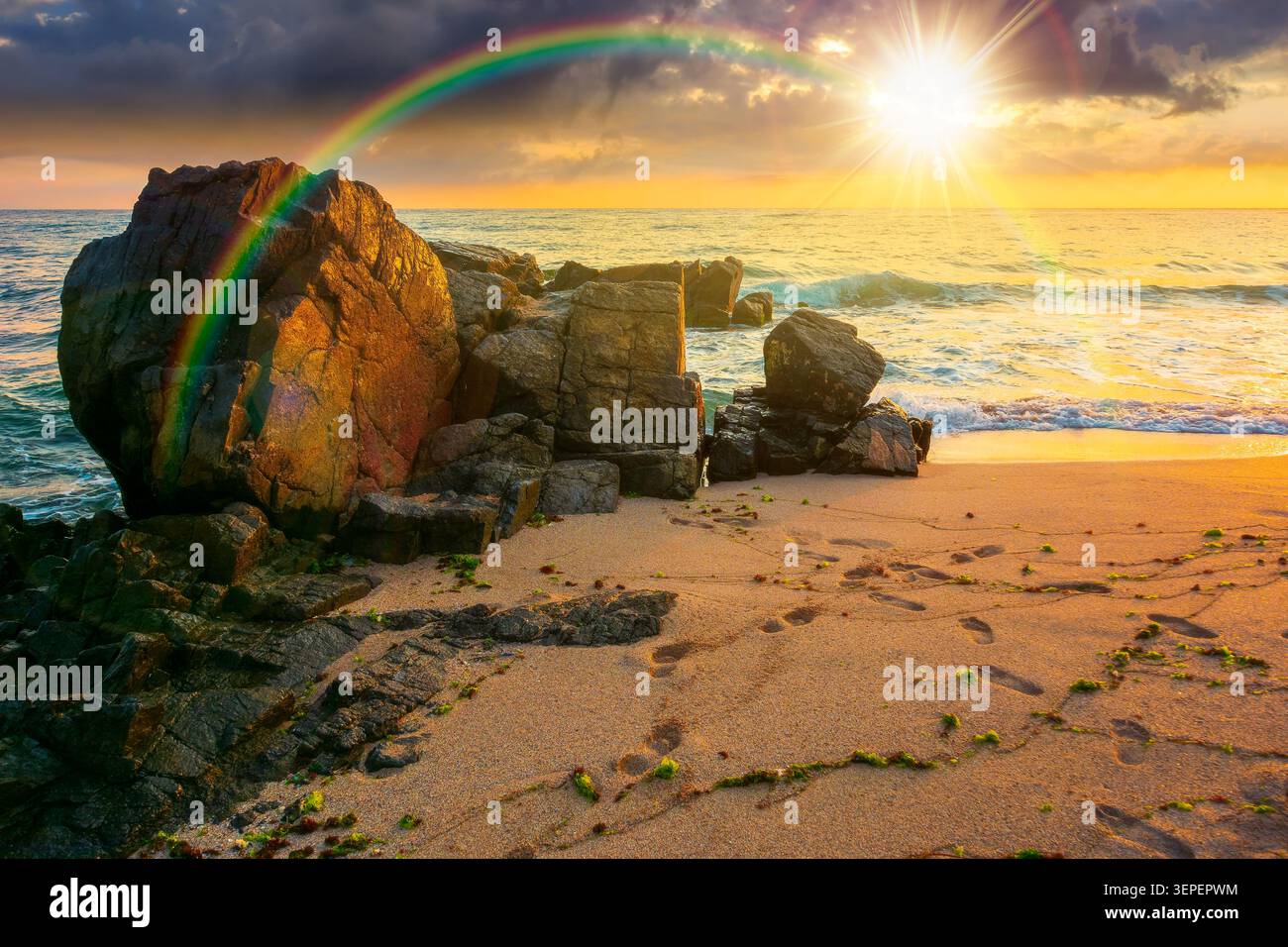 sunset over huge stones on the sandy beach. wonderful holiday season background at the sea. clouds on the blue sky above horizon. view of waves washin Stock Photo