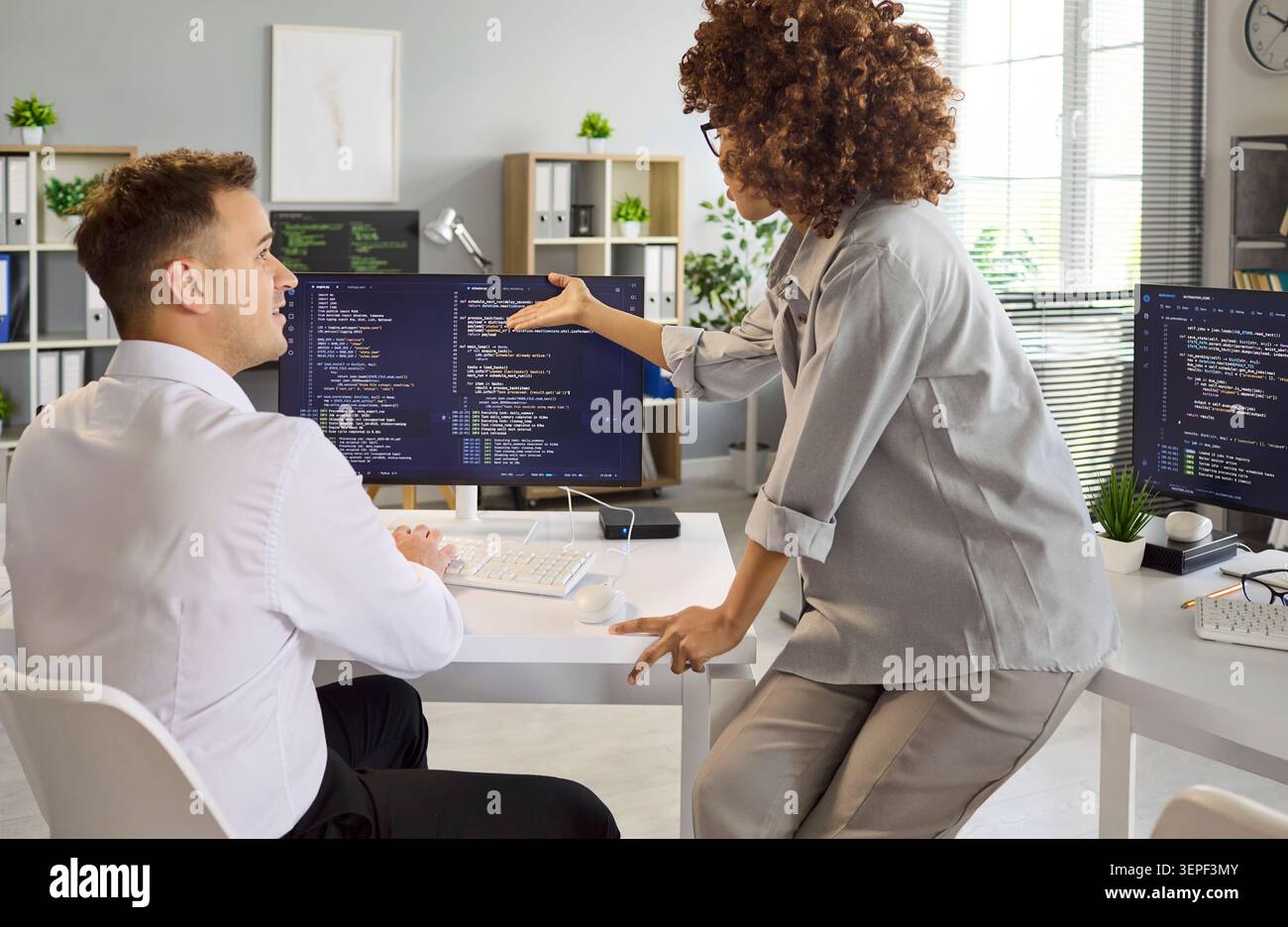 Software developers collaborating in office, reviewing code on dual monitors Stock Photo