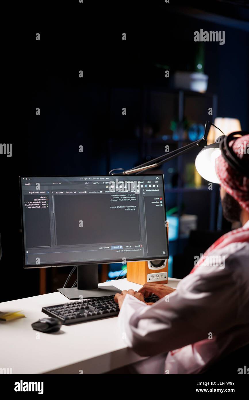 Traditional Middle Eastern developer compiles code on desktop computer, showcasing expertise in programming, algorithms, and software development; selective focus on pc monitor displaying source code. Stock Photo