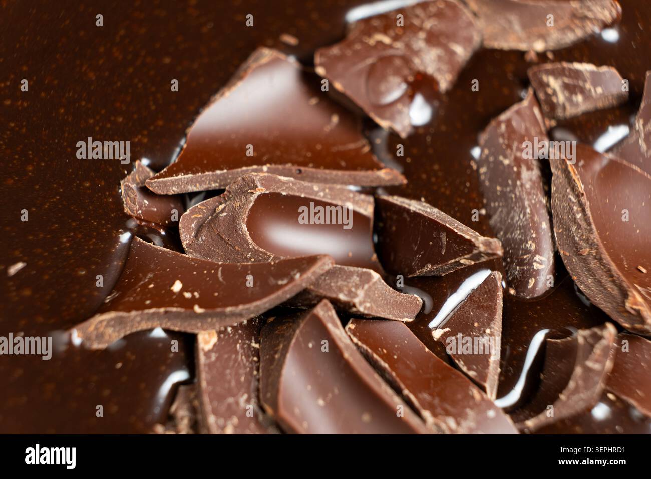 Dark chocolate chunks into liquid melted chocolate sauce background. Stock Photo