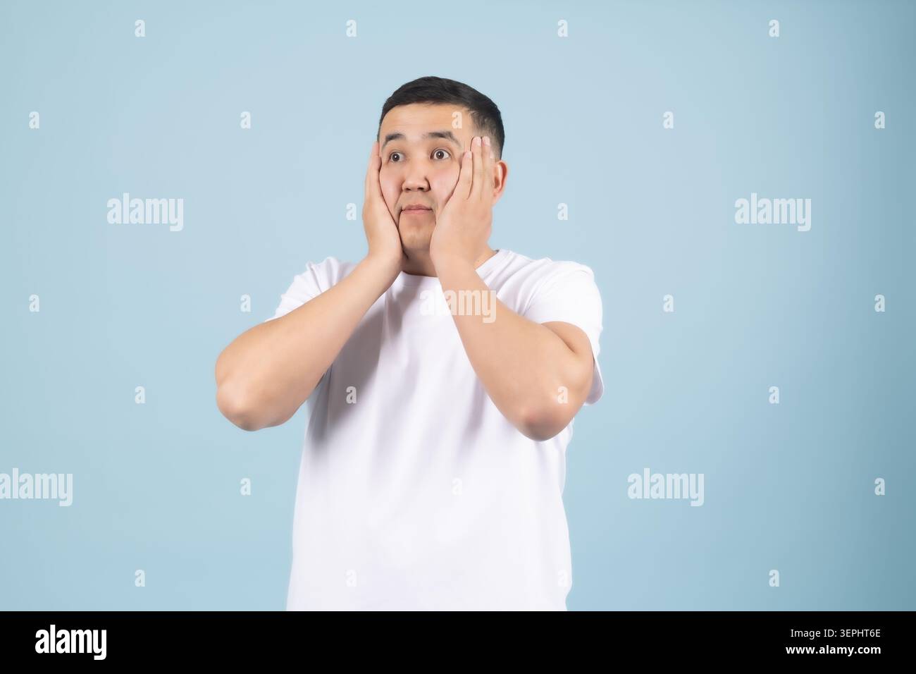 Young man holding both hands near face looking surprised and Stock Photo
