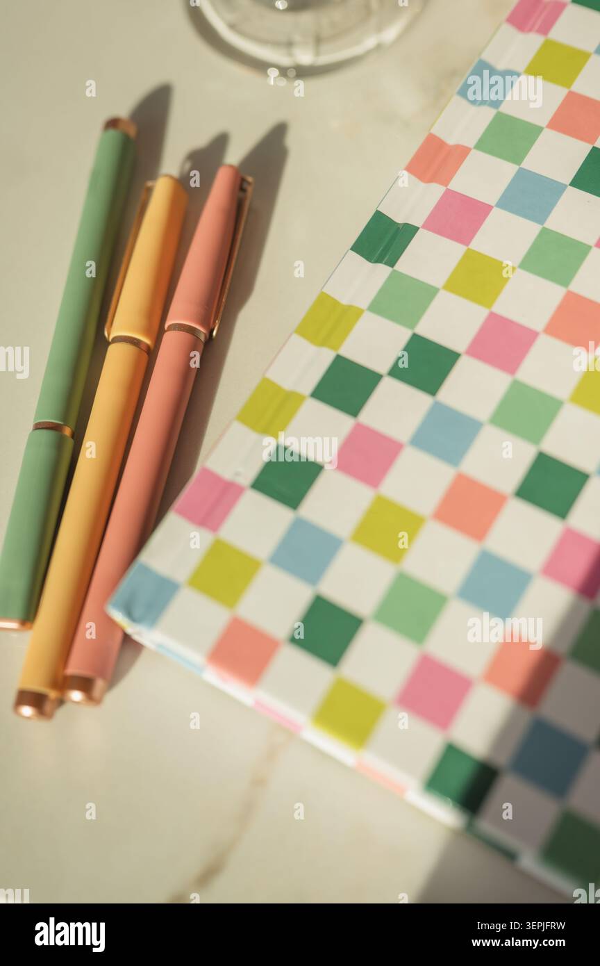 Colorful modern pens next to a checkered notebook in sunlight Stock Photo