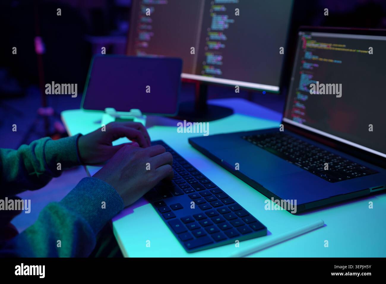 Programmer Typing Code on Laptop in Neon Lit Workspace Stock Photo