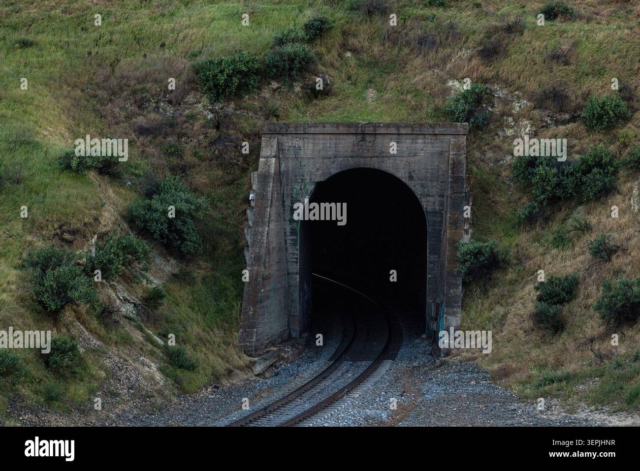 Train tracks lead into a dark mountain tunnel Stock Photo