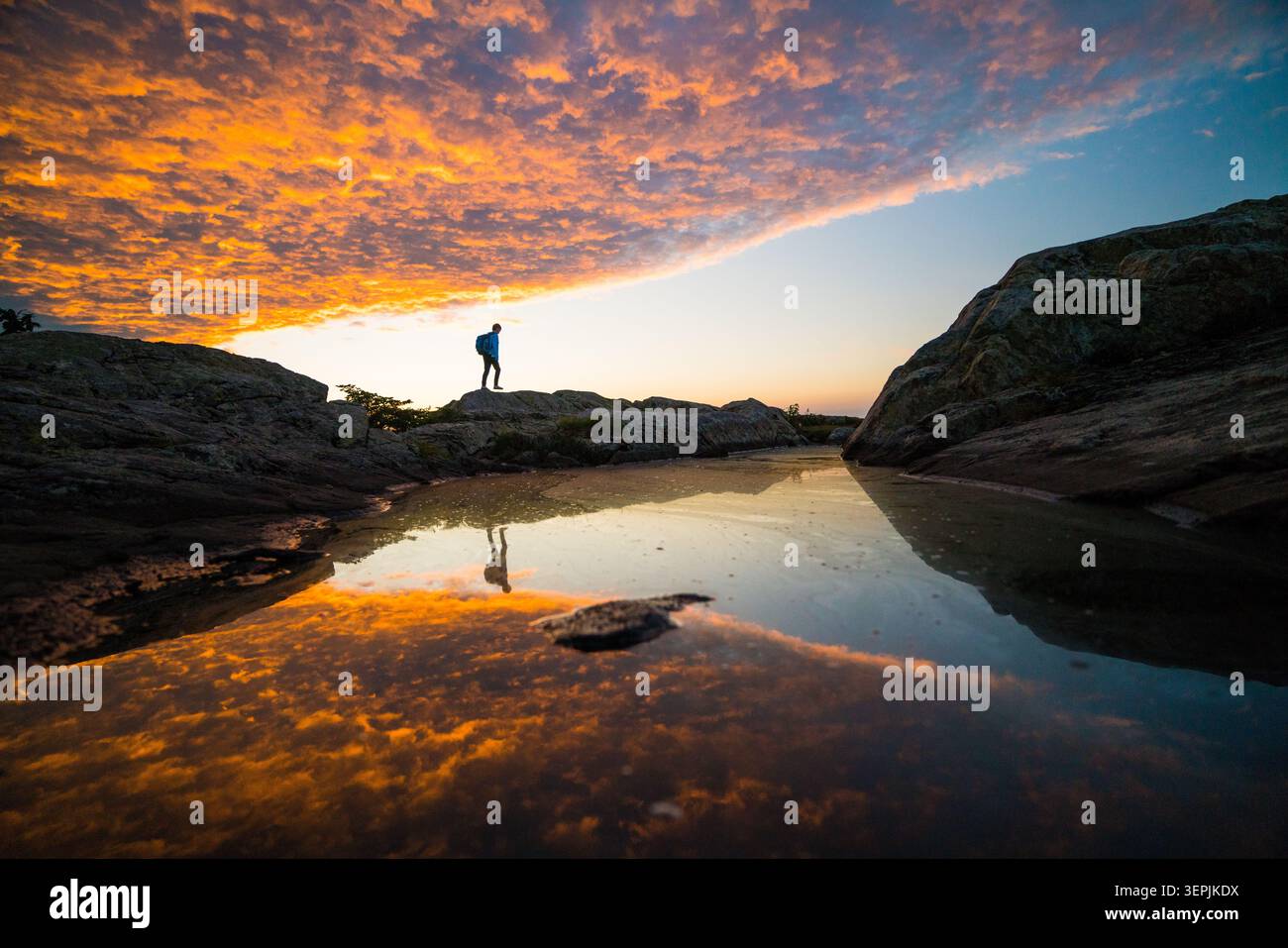 Hiker standing on rocks watching a dramatic sunset Stock Photo