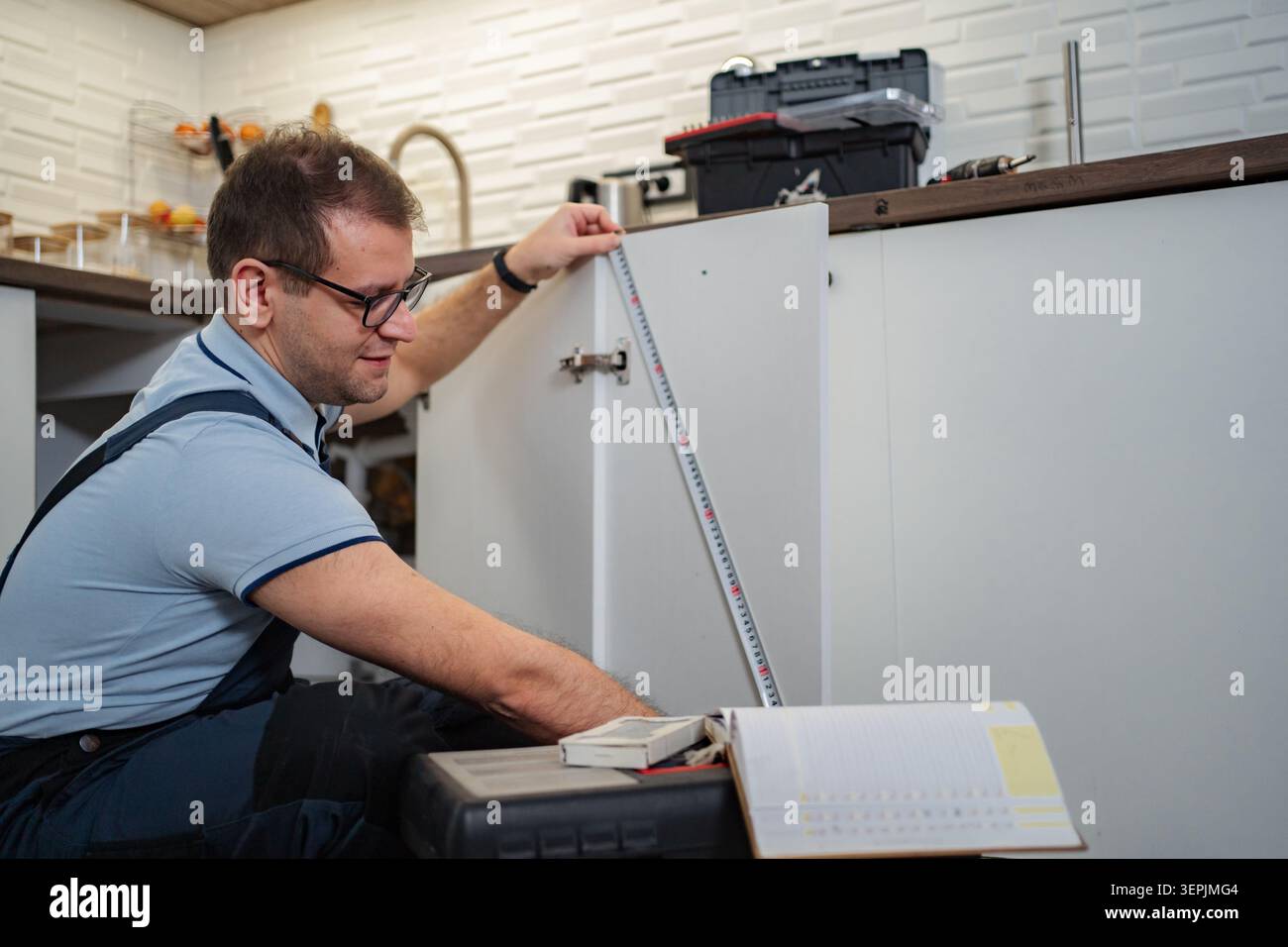 Man installing new kitchen cabinets using a measuring tape Stock Photo