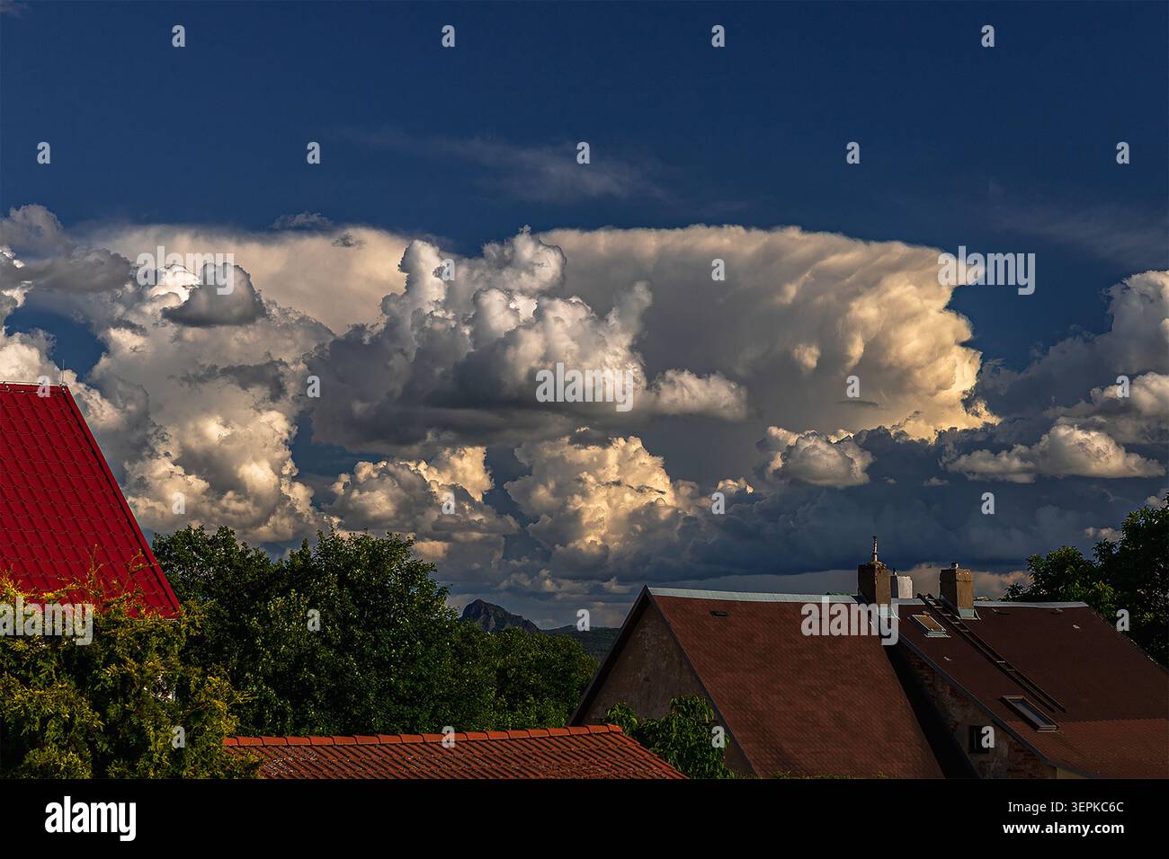 Dramatic cumulonimbus storm clouds forming over rural village houses under a deep blue sky Stock Photo