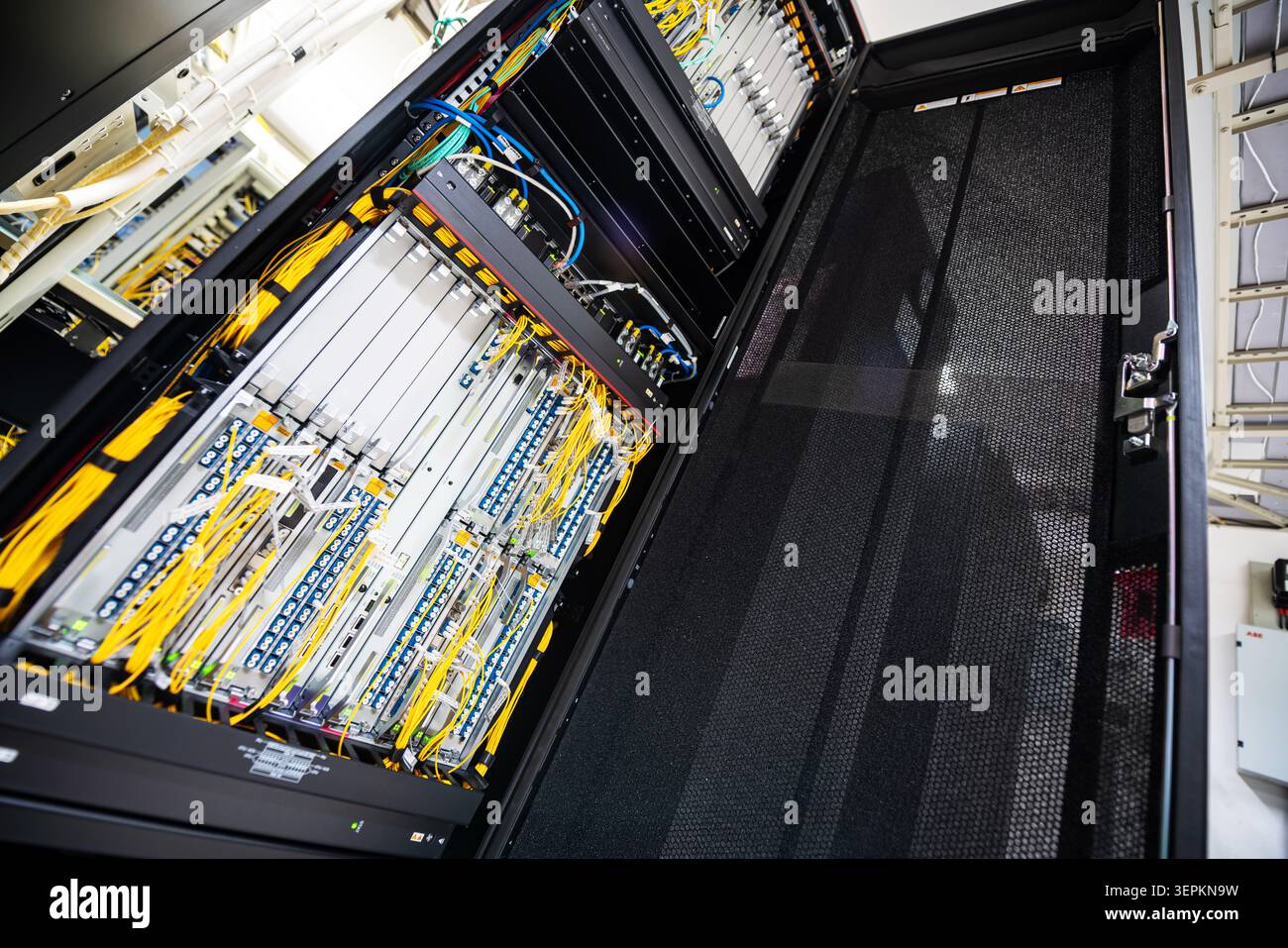 Close-up of high-density network switch chassis with fiber optic patch cords and cable labels in server room. Stock Photo