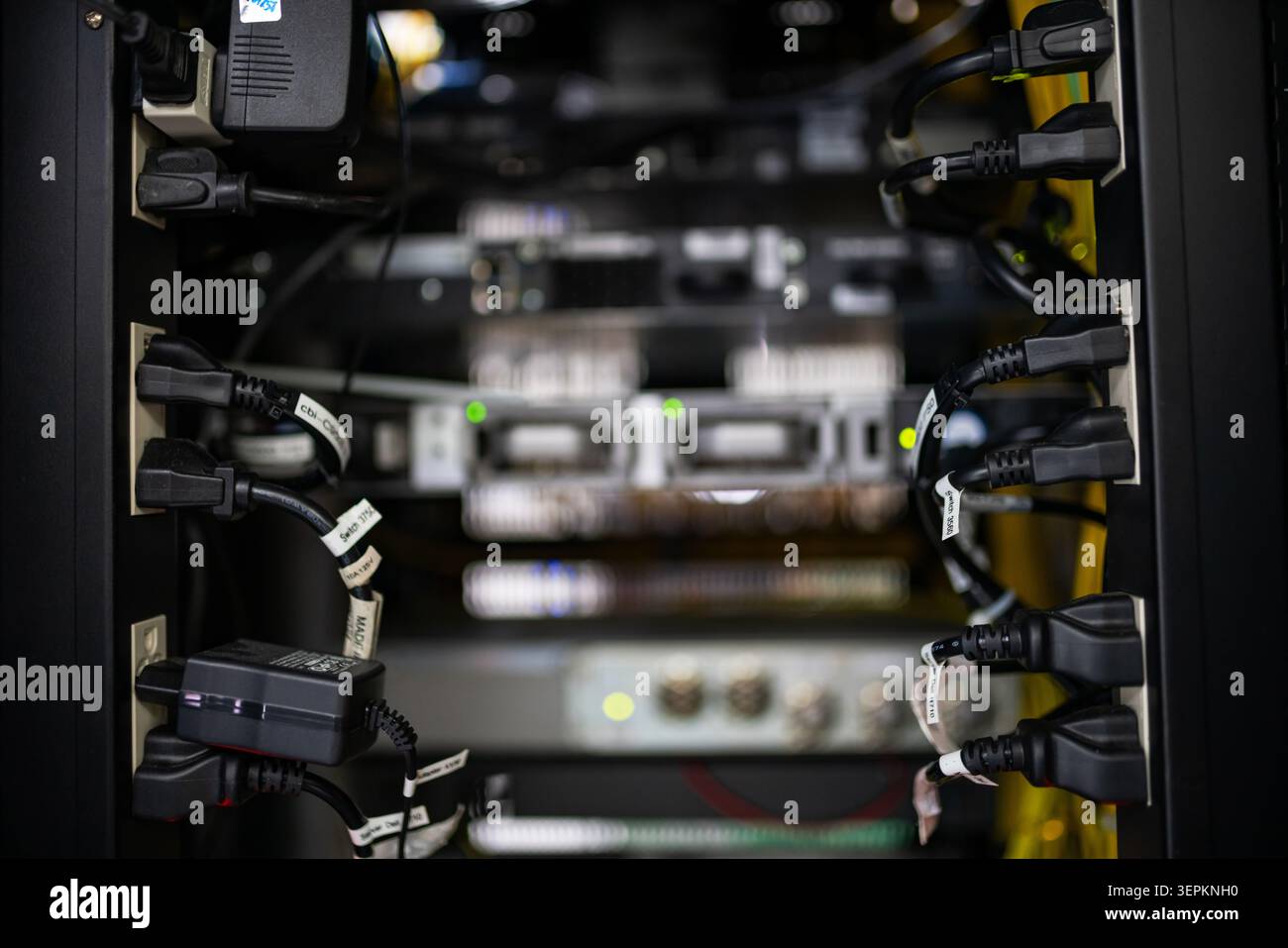 This image shows a professional data center with multiple server racks filled with electronic hardware, networking equipment, and connecting cables, e Stock Photo