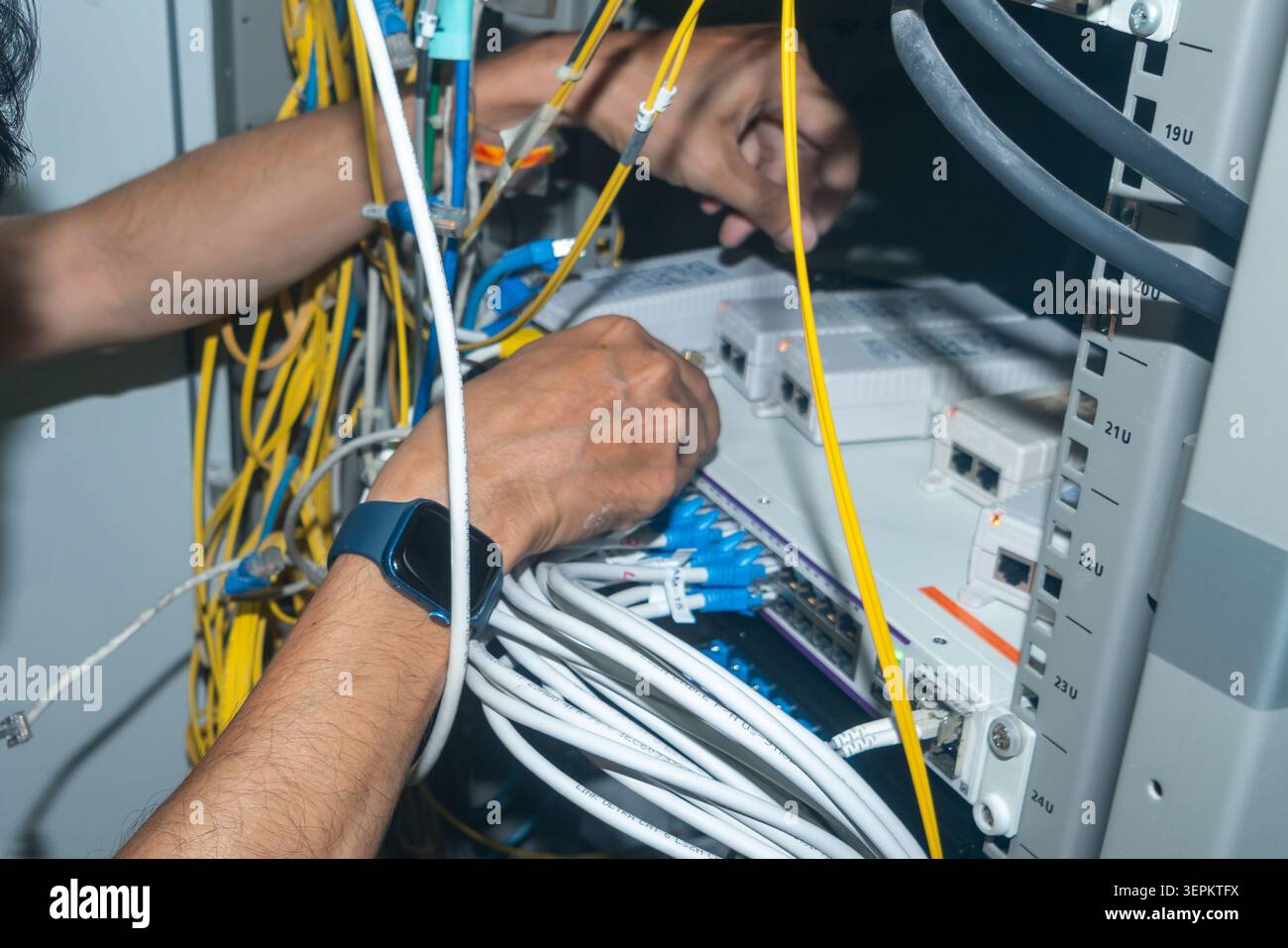 Two technicians are working on a complex network server setup with tangled cables and electronic components in a data center environment, focusing on Stock Photo