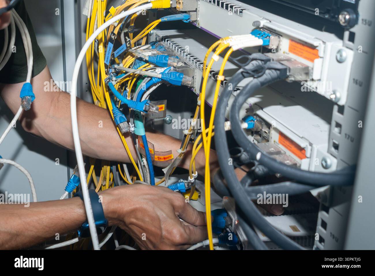 A technician working on a server rack with multiple network cables and hardware components, performing maintenance or setup in a data center or networ Stock Photo