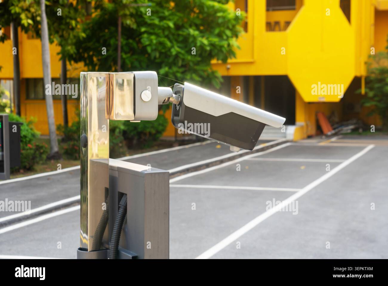 The image shows a modern outdoor security camera mounted on a metal stand, installed in a parking lot for surveillance, monitoring, and safety purpose Stock Photo