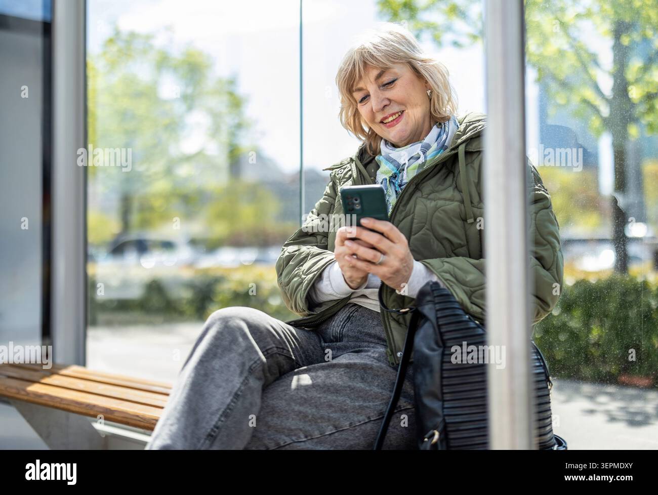 Woman using her smartphone while waiting for a bus in the city Stock Photo
