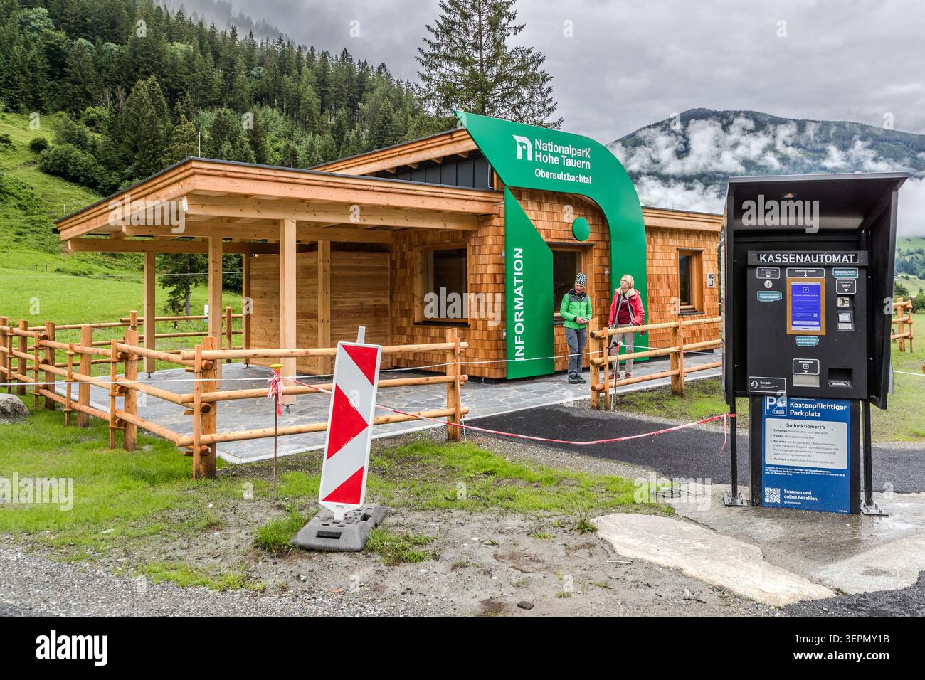 Two women are standing at the newly built Obersulzbachtal National Park Information Centre on Mittergasse. A pay-at-machine next to it handles the parking charges. Mittergasse, Sulzau, Rosental, Neukirchen am Großvenediger, Bezirk Zell am See, Salzburg, 5741, Austria Stock Photo