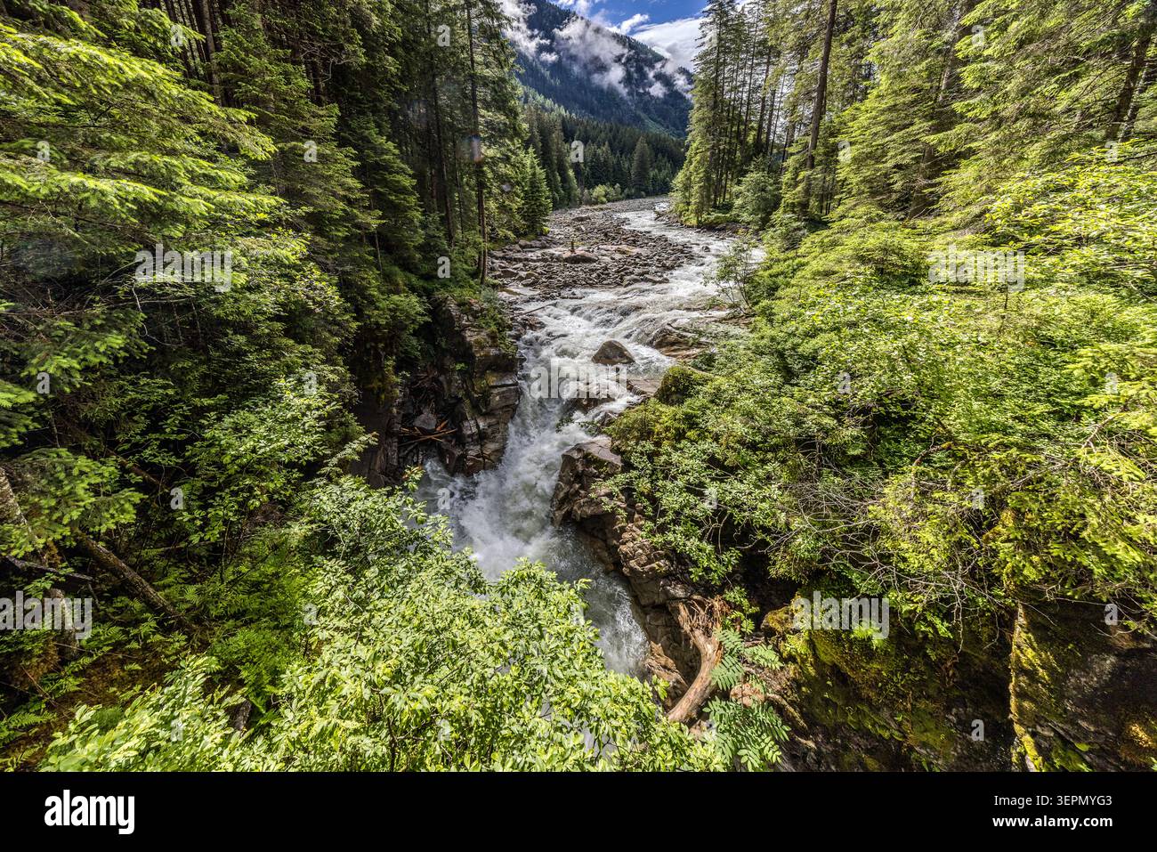 The Untersulzbach carries a powerful flow of water through the narrow rocky gorge on the Waterfall Circular Walk in the Untersulzbach Valley; in the background, clouds hang over the peaks of the Hohe Tauern National Park. Sulzau, Rosental, Neukirchen am Großvenediger, Bezirk Zell am See, Salzburg, 5741, Austria Stock Photo