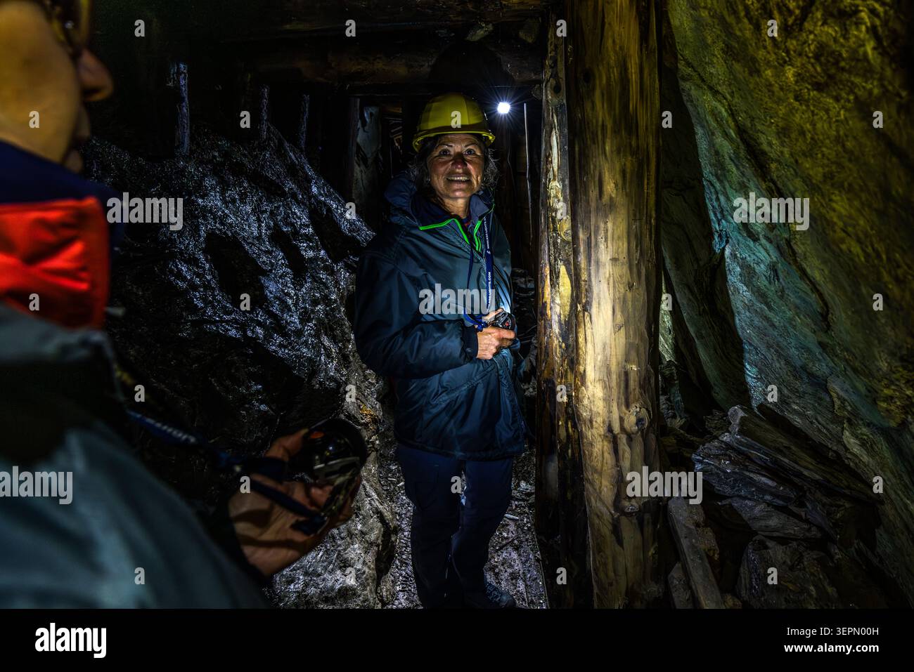 A participant on the guided tour smiles in a narrow section of the Hochfeld exhibition mine, supported by wooden beams. Her helmet lamp illuminates the narrow passageway in the former copper mine in the Untersulzbachtal valley. Rosental, Neukirchen am Großvenediger, Bezirk Zell am See, Salzburg, 5741, Austria Stock Photo