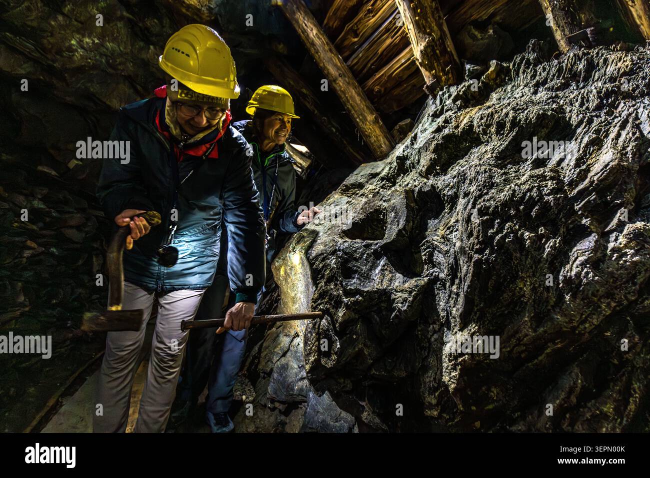 Two participants on the guided tour are using a hammer and a helmet lamp to examine a hollowed-out rock formation in the Hochfeld exhibition mine, traces of historic ore mining in the Untersulzbachtal valley. Rosental, Neukirchen am Großvenediger, Bezirk Zell am See, Salzburg, 5741, Austria Stock Photo