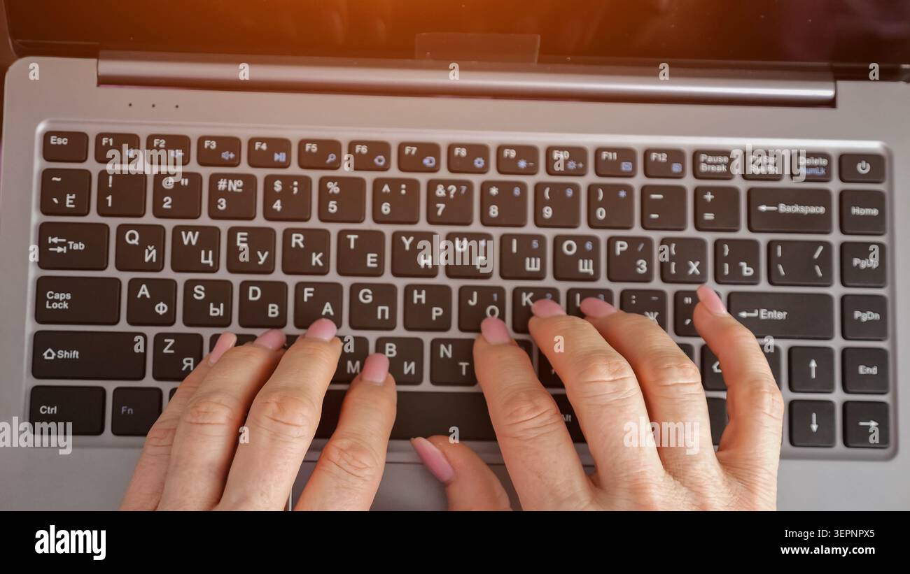 Female hands with pink nails typing on a laptop keyboard at a desk, close up top view showing focused digital work, communication, and remote Stock Photo