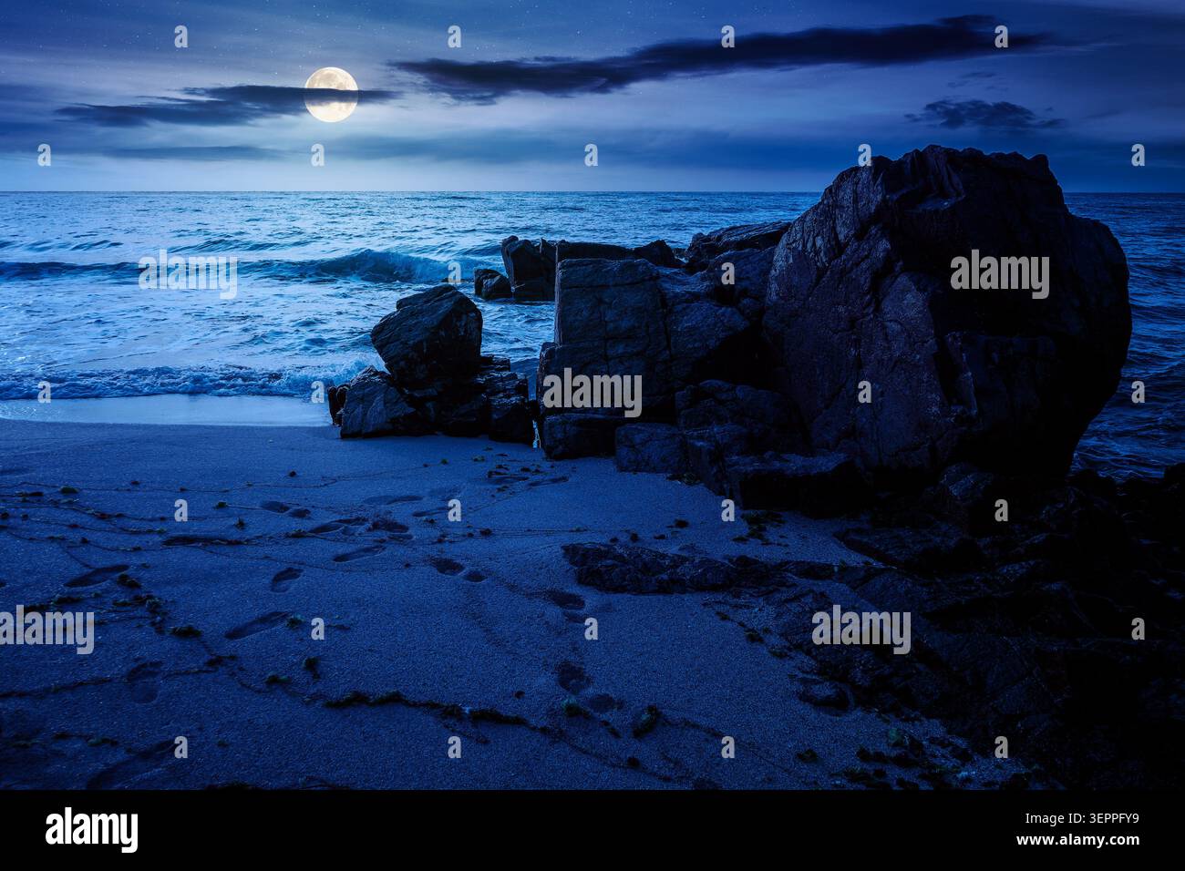 huge stones on the sandy beach at night. mysterious holiday season background at the sea. full moon over clouds on the dark sky above horizon. view of Stock Photo