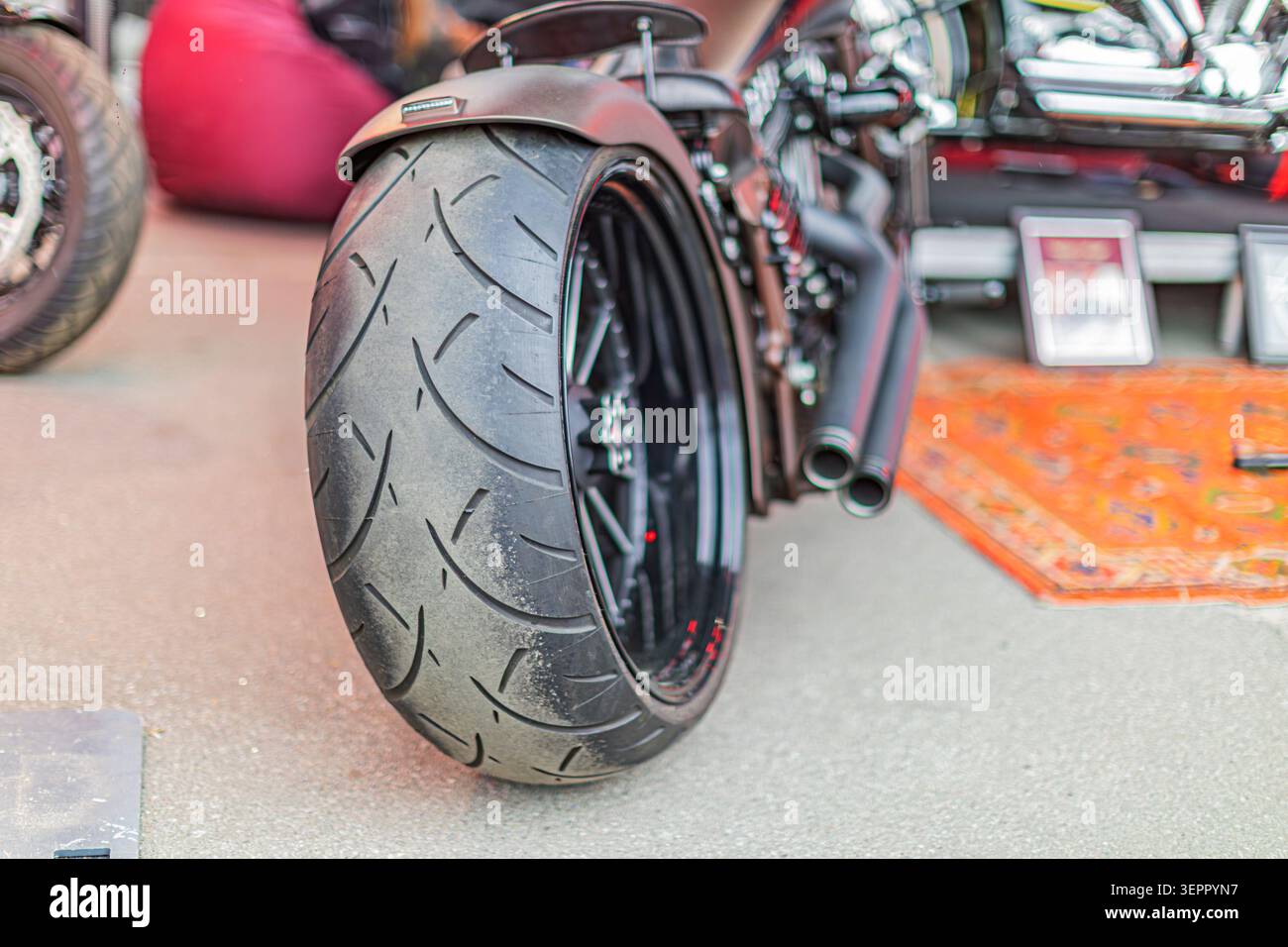 Modern high-performance motorcycle rear view showcasing deep-dish wheel design, textured black tire, red hub accent, polished chrome exhaust pipes, an Stock Photo