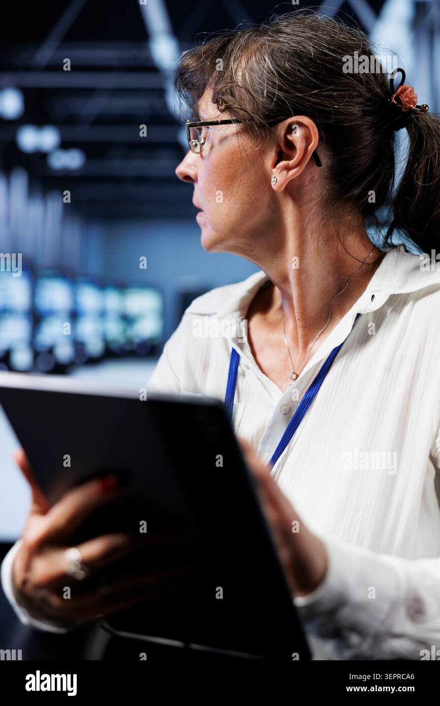 Old computer scientist updating data center rackmounts, writing intricate binary code scripts on tablet, using programming to fortify cybersecurity in technically advanced supercomputer hub. Stock Photo