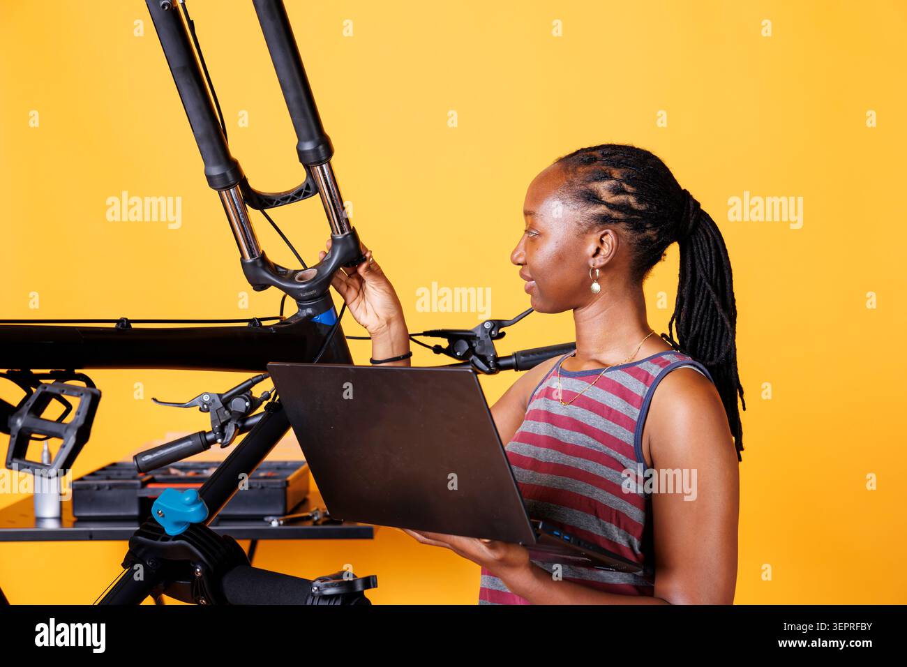 Determined African American female utilizing laptop for bike maintenance research. Stock Photo