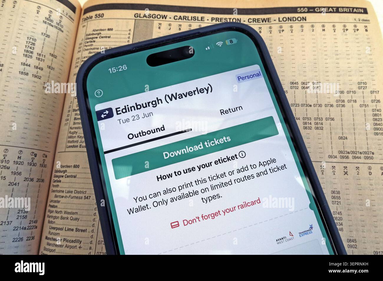The Trainline digital rail ticket for an Edinburgh Waverley journey displayed on an iPhone resting on a West Coast Main Line timetable. Stock Photo