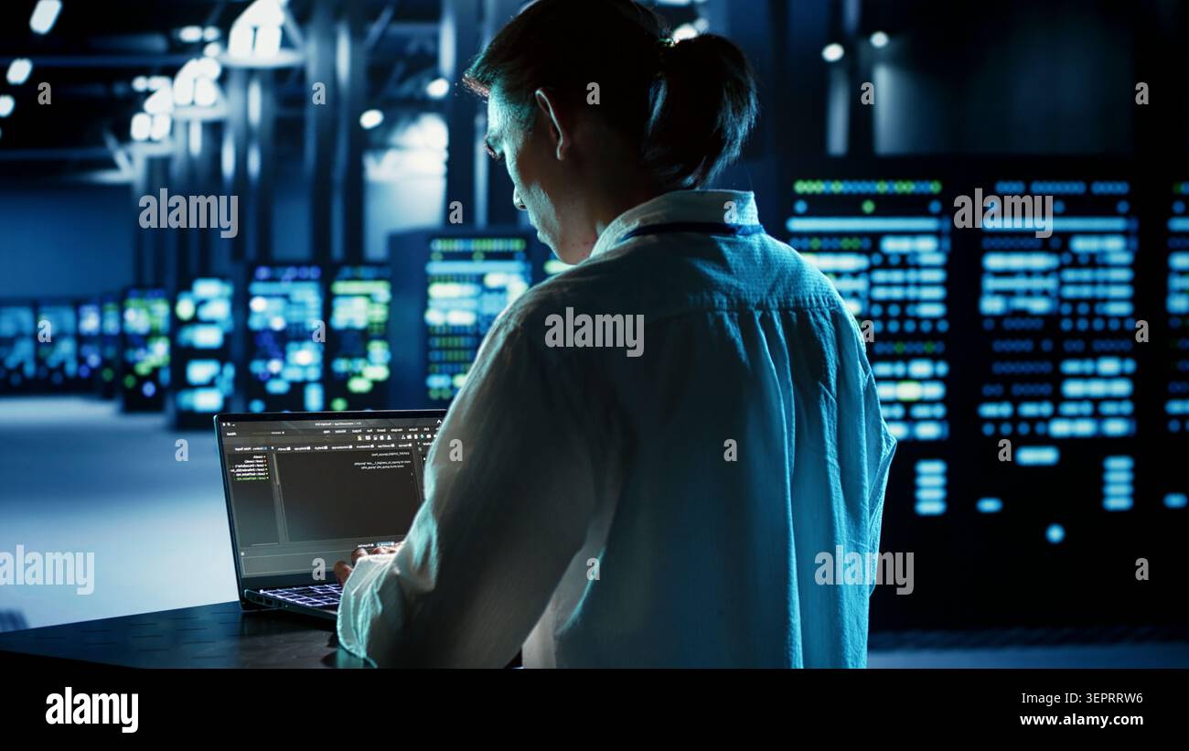 Experienced engineer running programming code on laptop, troubleshooting and updating data center equipment designed to accommodate server clusters, networking systems and storage arrays. Stock Photo