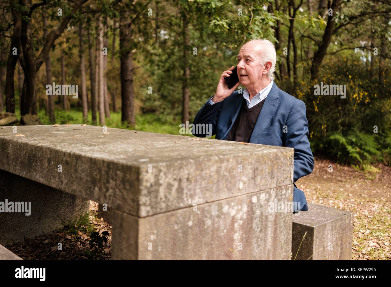 Senior man using a smartphone for communication outdoors sitting at a stone table Stock Photo