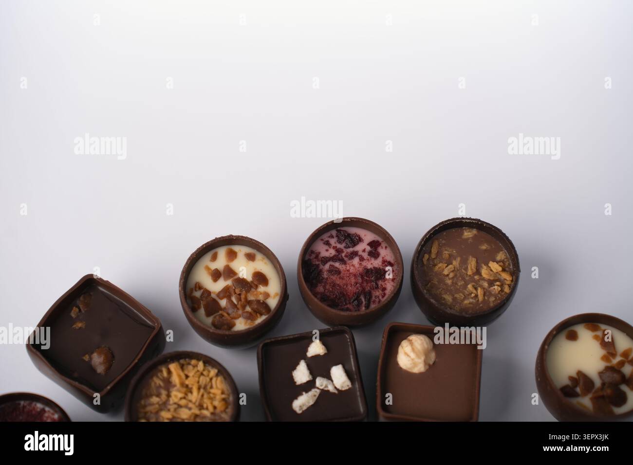 assorted artisanal chocolate bonbons and truffles arranged in a neat row on a clean white background, highlighting glossy milk and dark shells, creamy Stock Photo