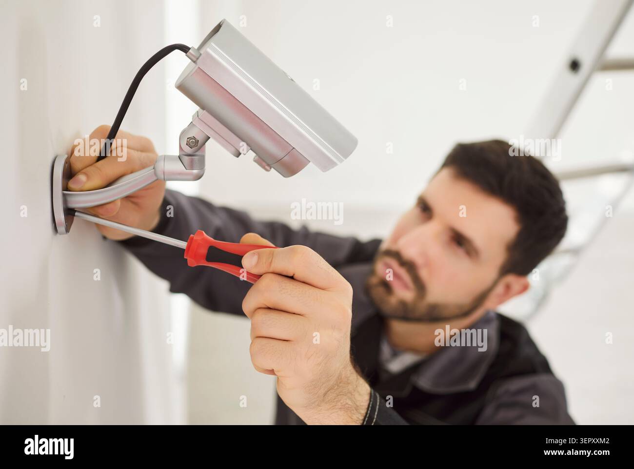 Professional service man installing security camera, using screwdriver tool, fastening mount to wall Stock Photo