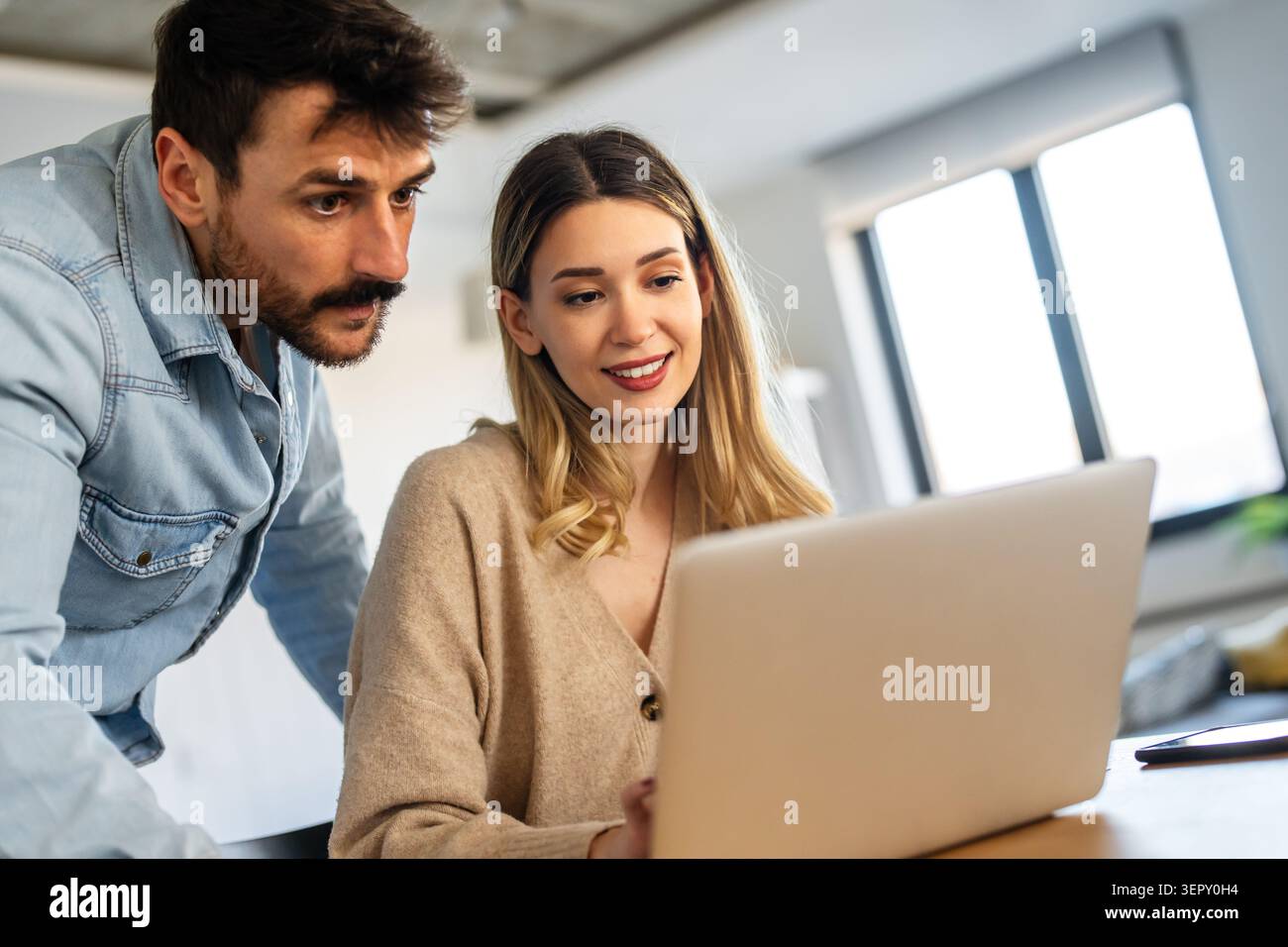 Young happy multiethnic couple having fun while using laptop, digital device at home Stock Photo