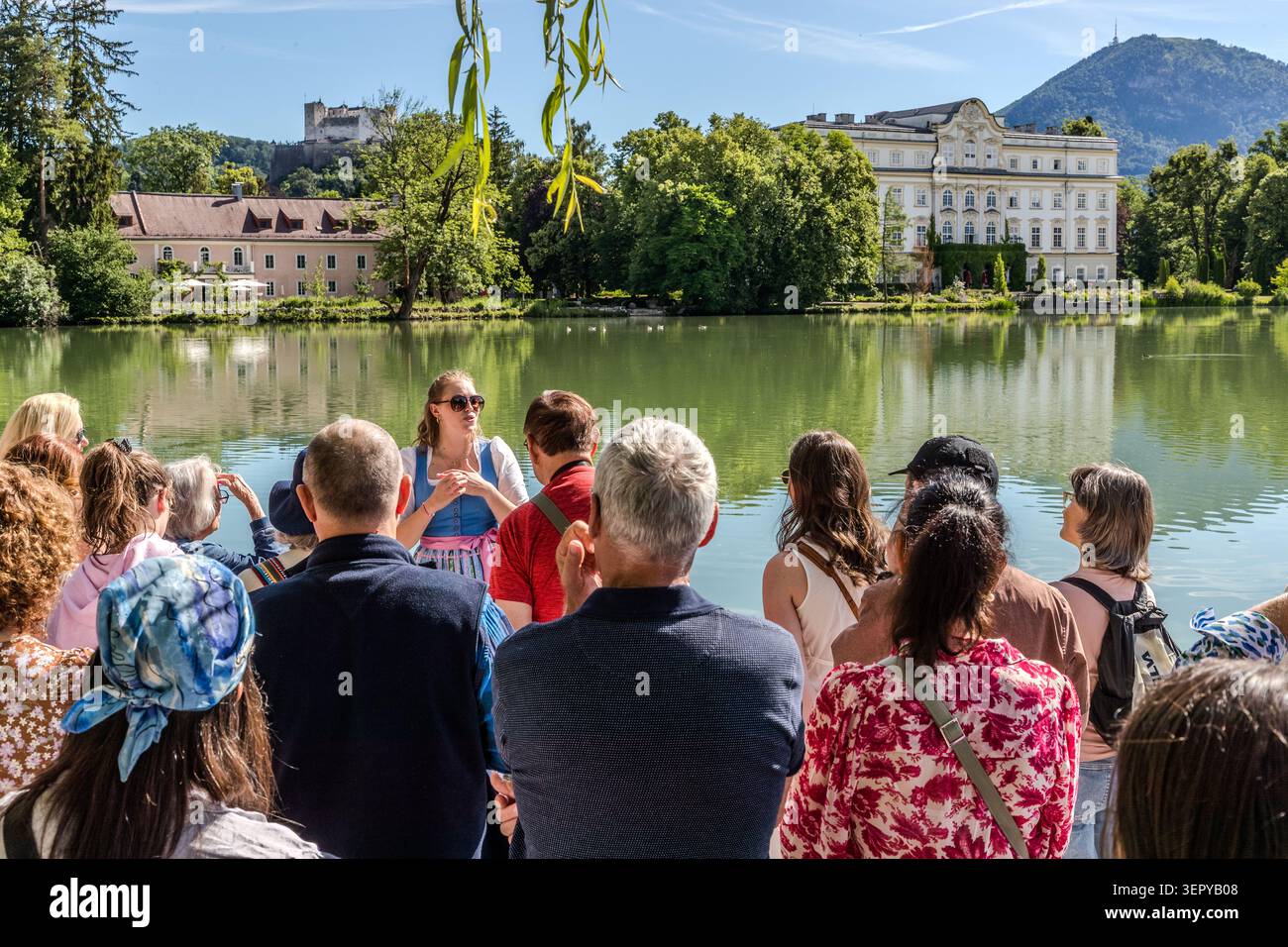 Tour guide Stephanie Hinterbuchner is explaining the area around the Leopoldskron Pond to a group; in the background are Leopoldskron Palace and Hohensalzburg Fortress. The Baroque palace served as the outdoor setting for the Trapp family’s estate in the film ‘The Sound of Music’ (1965). Salzburg, Austria Stock Photo