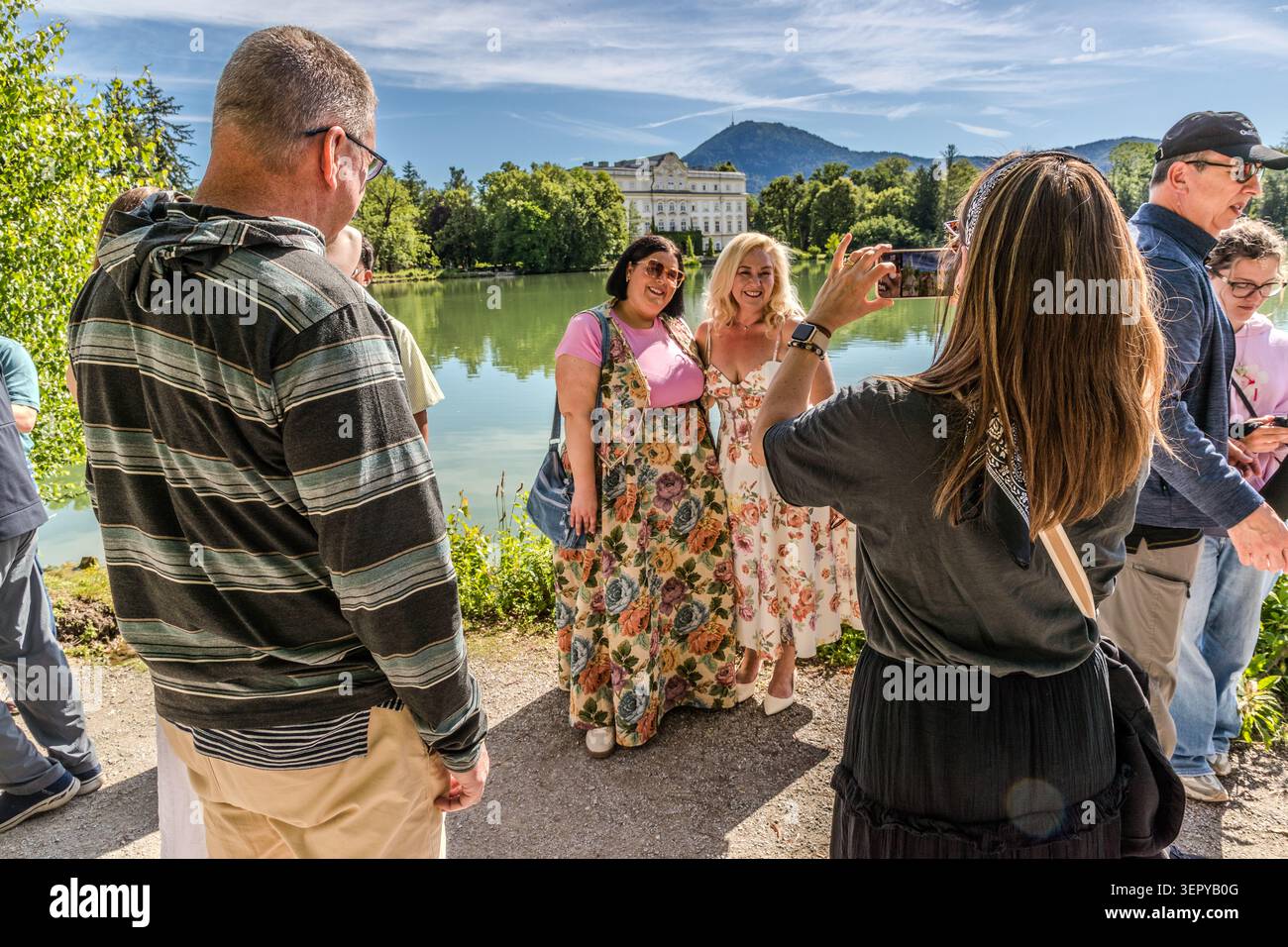Female tourists have their photograph taken in front of the Leopoldskroner Weiher, with Leopoldskron Palace in the background. The 18th-century Baroque palace is one of the most famous locations from the film *The Sound of Music*. Salzburg, Austria Stock Photo