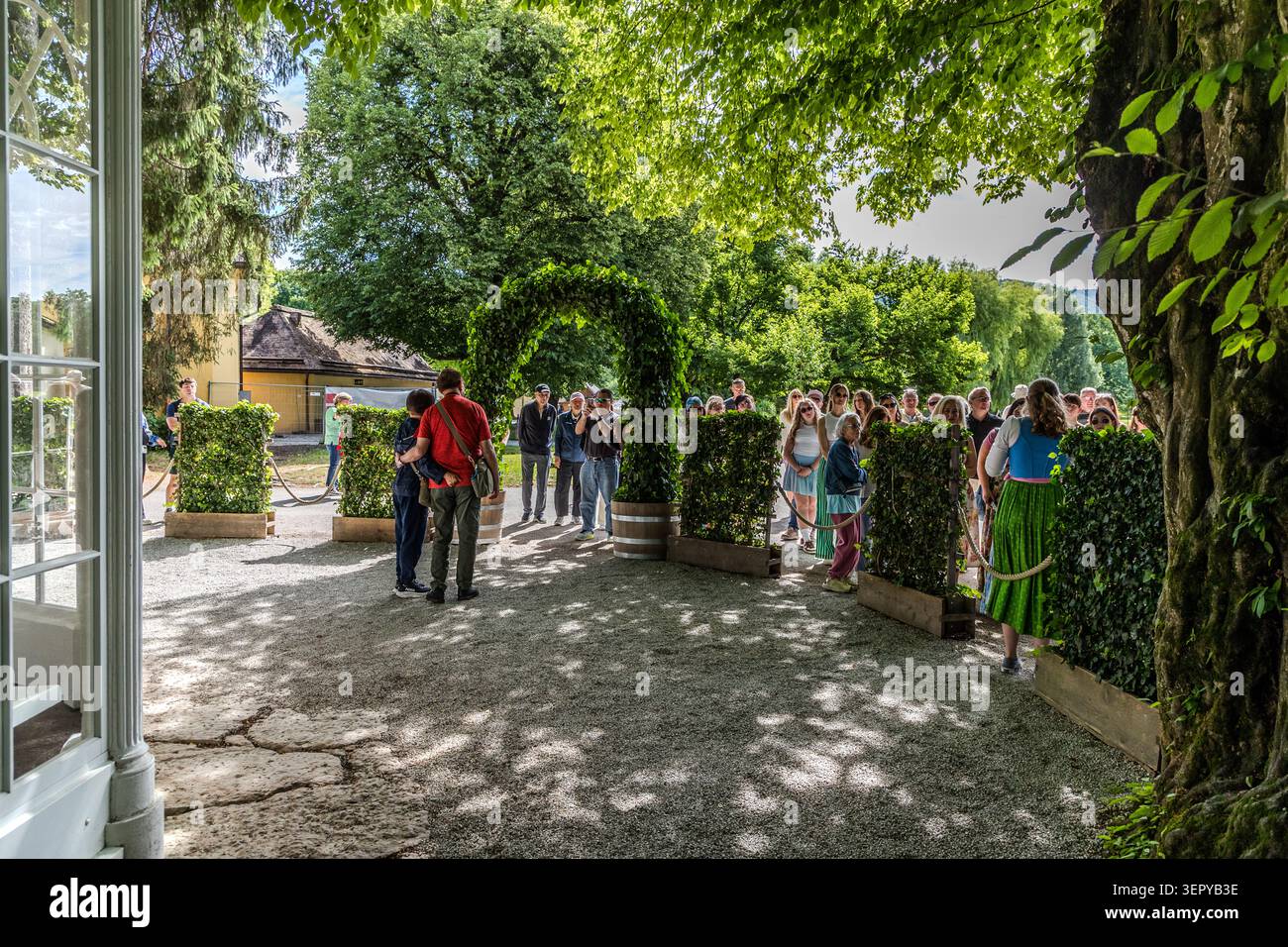 Visitors on the “Sound of Music Tour” pass through a leafy archway in the grounds of Leopoldskron Palace in Salzburg. The early 18th-century Baroque palace served as the outdoor setting for the von Trapp family’s terraced garden in the 1964 Hollywood film *The Sound of Music* (directed by Robert Wise, 1965). Salzburg, Austria Stock Photo