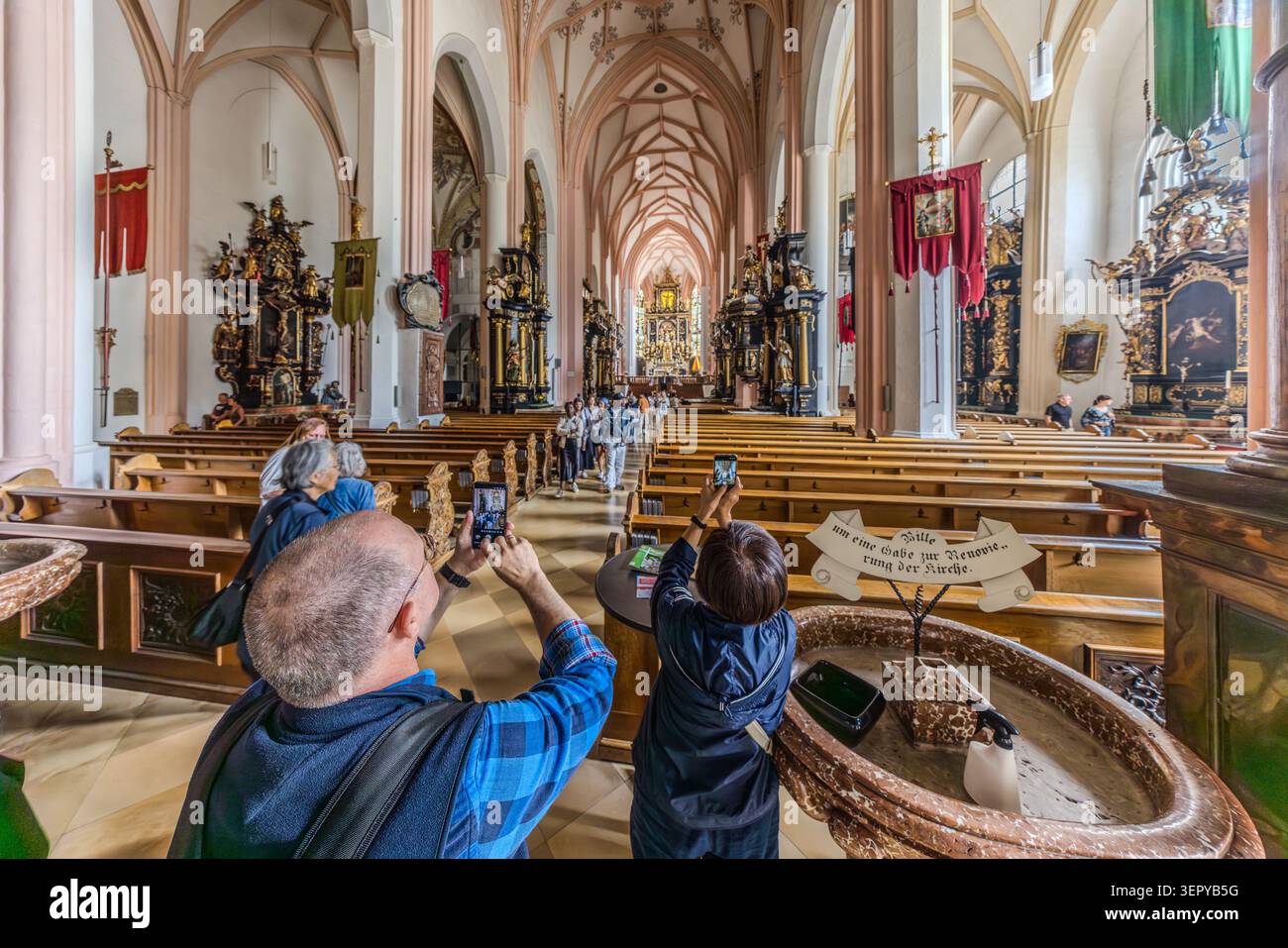 Interior of St Michael’s Basilica in Mondsee (Salzkammergut, Upper Austria): This three-nave church, with its Gothic ribbed vaults and Baroque side altars, gained international fame thanks to the wedding scene in the film musical ‘The Sound of Music’ (1965, directed by Robert Wise). In the foreground is the Baroque baptismal font; visitors are taking photographs of the nave. Mondsee, Schlößl, Upper Austria Stock Photo
