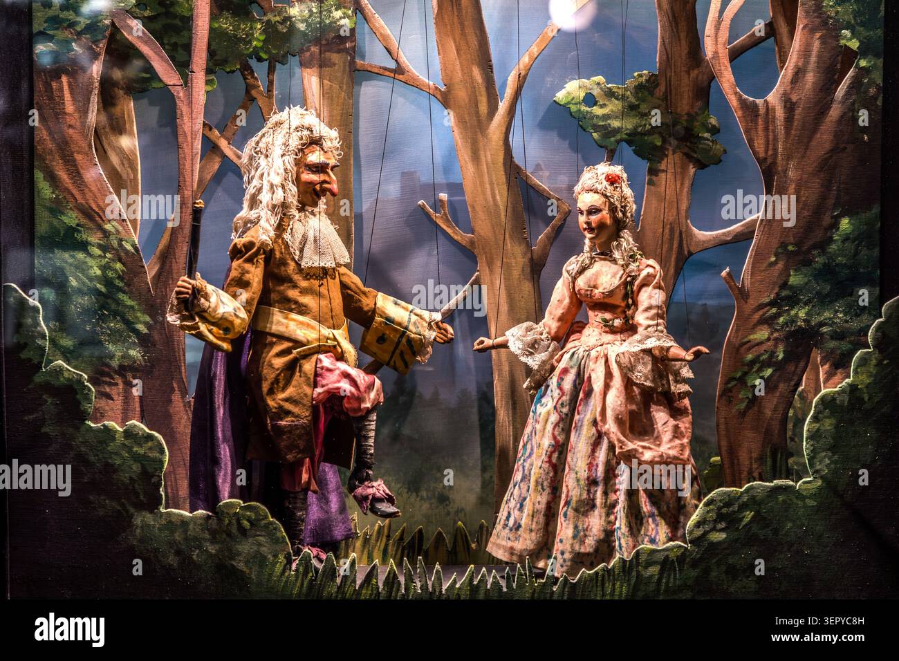 Two marionettes on the stage of the Salzburg Marionette Theatre (Schwarzstraße 24) against a painted forest backdrop: a gentleman wearing a long wig and a baroque costume, and a lady in a pink dress. The theatre regularly stages works by Mozart and other composers as part of its repertoire. Salzburg, Austria Stock Photo