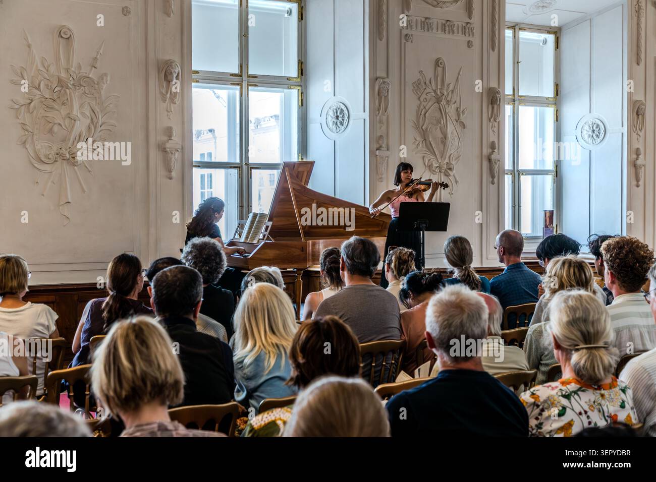 Chamber concert at the DomQuartier in Salzburg: Two musicians – one playing the historic fortepiano, the other the violin – perform before a seated audience in a hall featuring Baroque stucco decoration and tall lattice windows. The DomQuartier organises chamber concerts in the historic state rooms of the Archbishop’s Residence. Residenzplatz, Salzburg, Austria Stock Photo