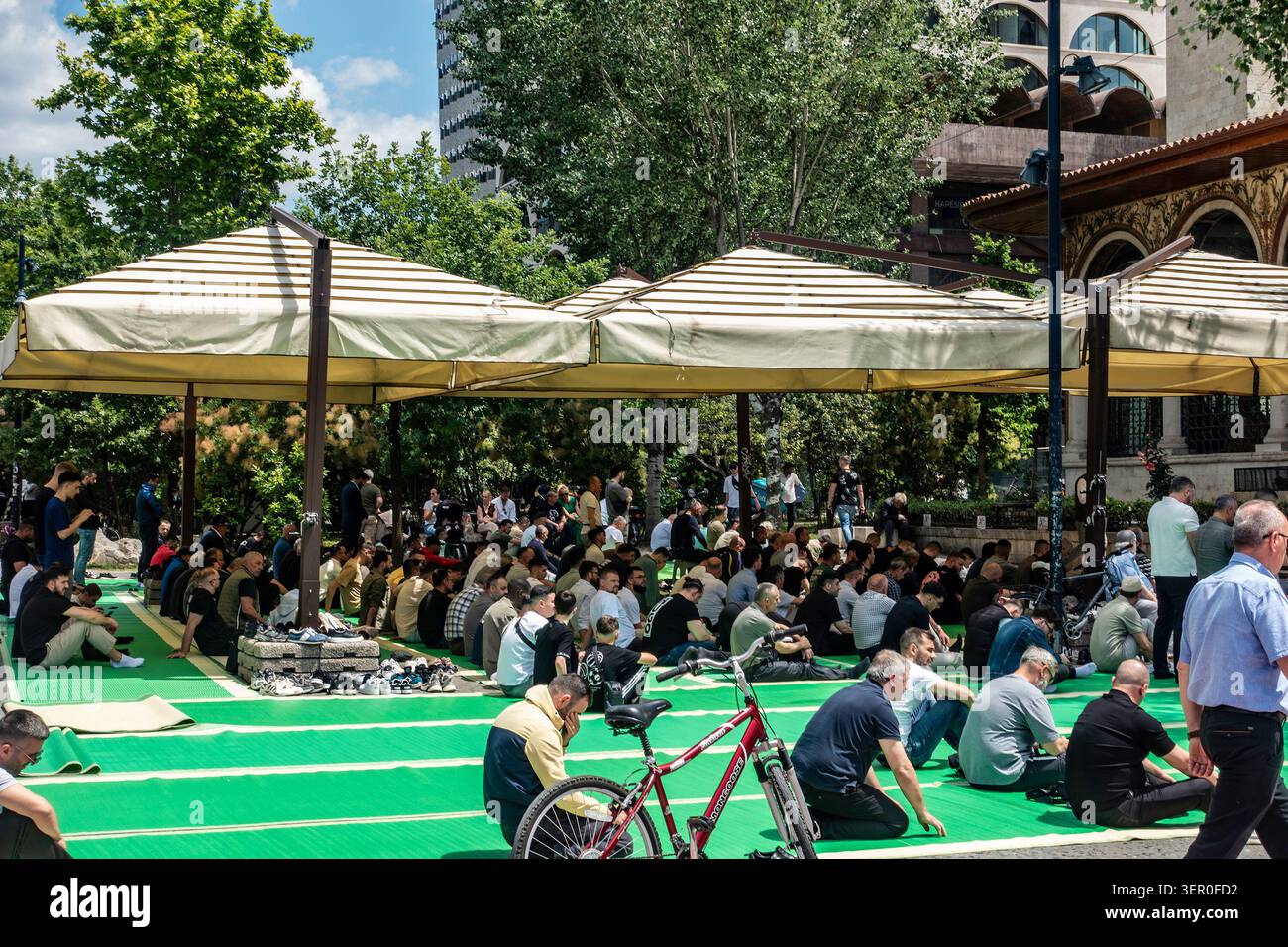 Muslim men gathered for outdoor Friday prayer on green mats under large beige umbrellas next to the Et'hem Bey Mosque in Tirana, Albania. Stock Photo